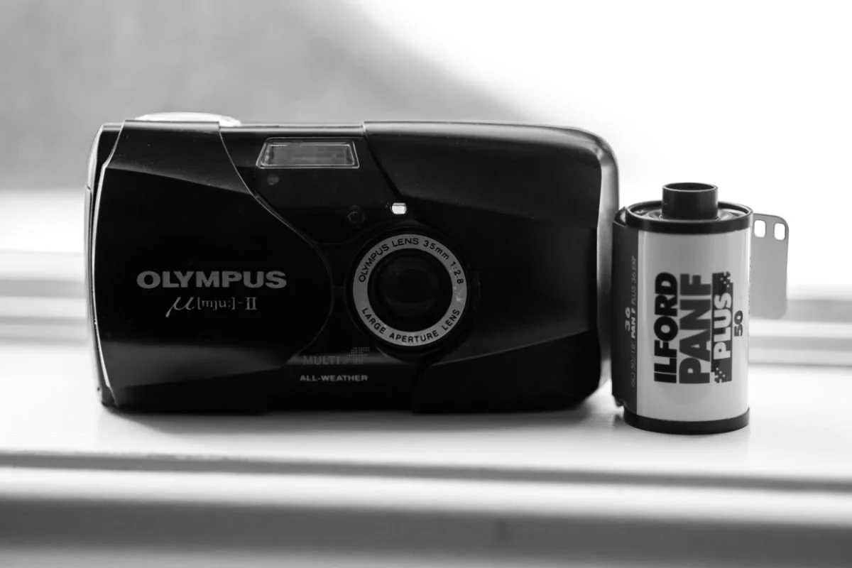 A black vintage Olympus cardboard camera with a film roll beside it.