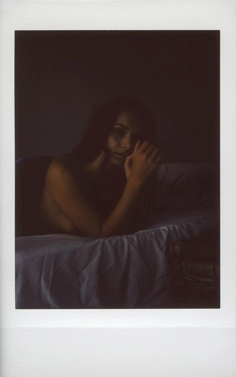 A woman lying on a bed in a dark room, partially covering her face with her hand, with dim lighting