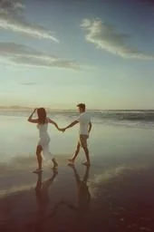 A couple holding hands and walking on the beach near the water at sunset