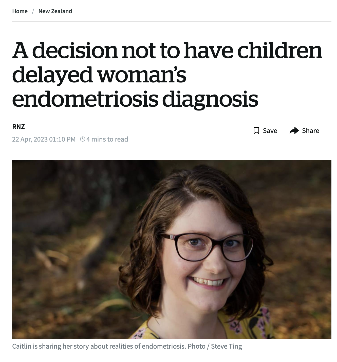 A woman with shoulder-length brown hair, glasses, and a yellow floral top smiling outdoors in a wooded area.