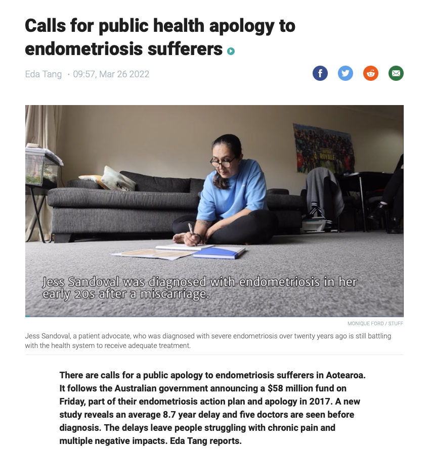 Woman sitting on carpeted floor writing in notebooks with a sofa, chair, and colorful poster in background.