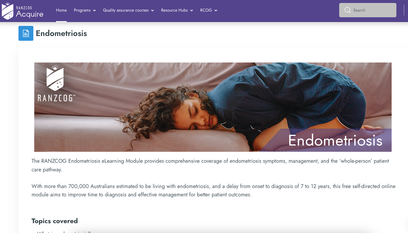 A woman lying on her side on a bed, appearing to be in discomfort, with a serious or tired expression, wearing a dark shirt and resting her head on a pillow.