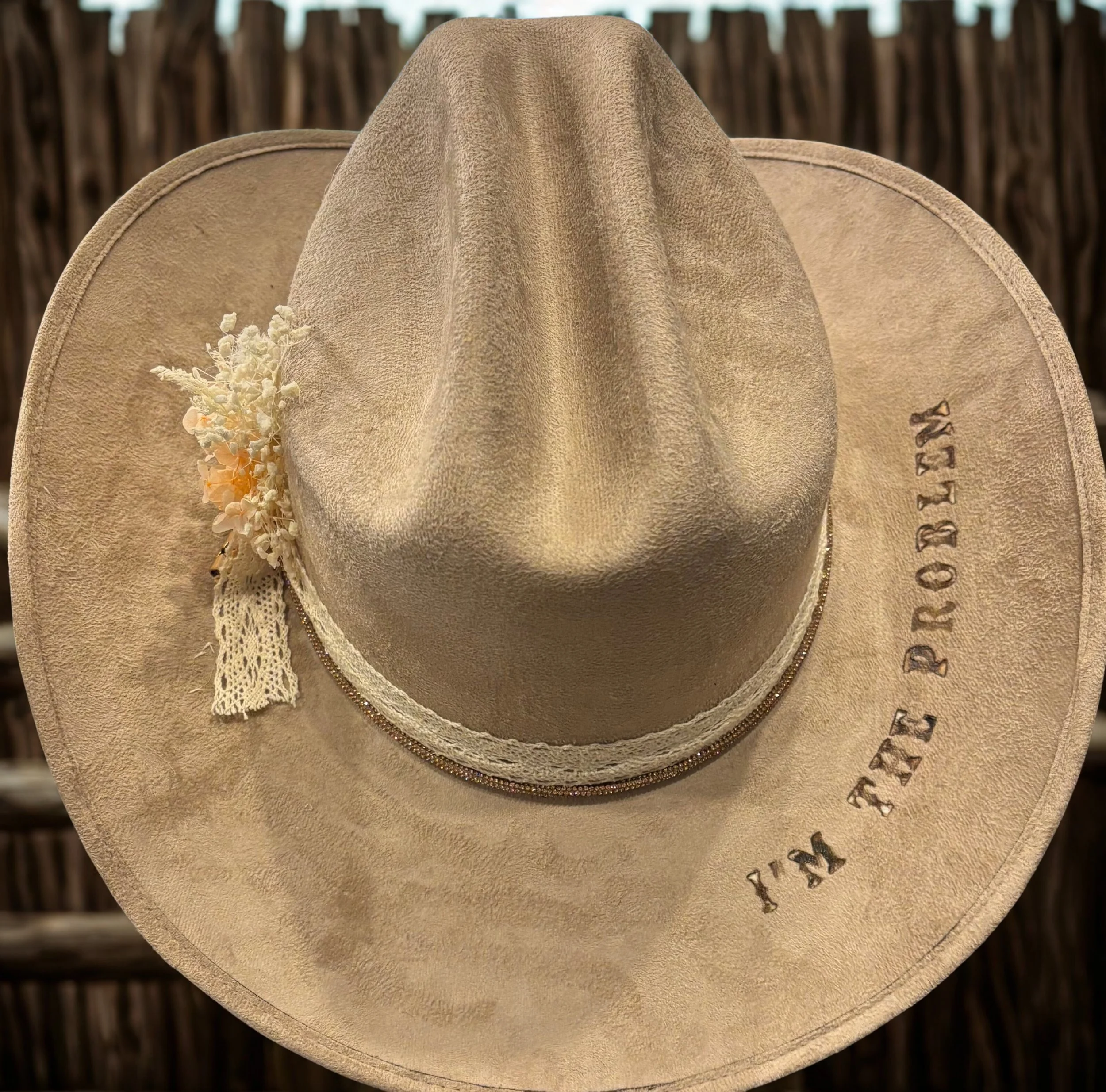A beige cowboy hat with a decorative band, a small floral arrangement, lace, and the words "FTX FOREVER" embroidered on the brim