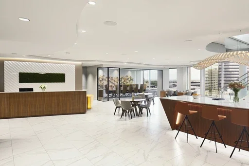 Modern, bright lounge area with a reception desk, dining table, and bar with stools in a high-rise building.