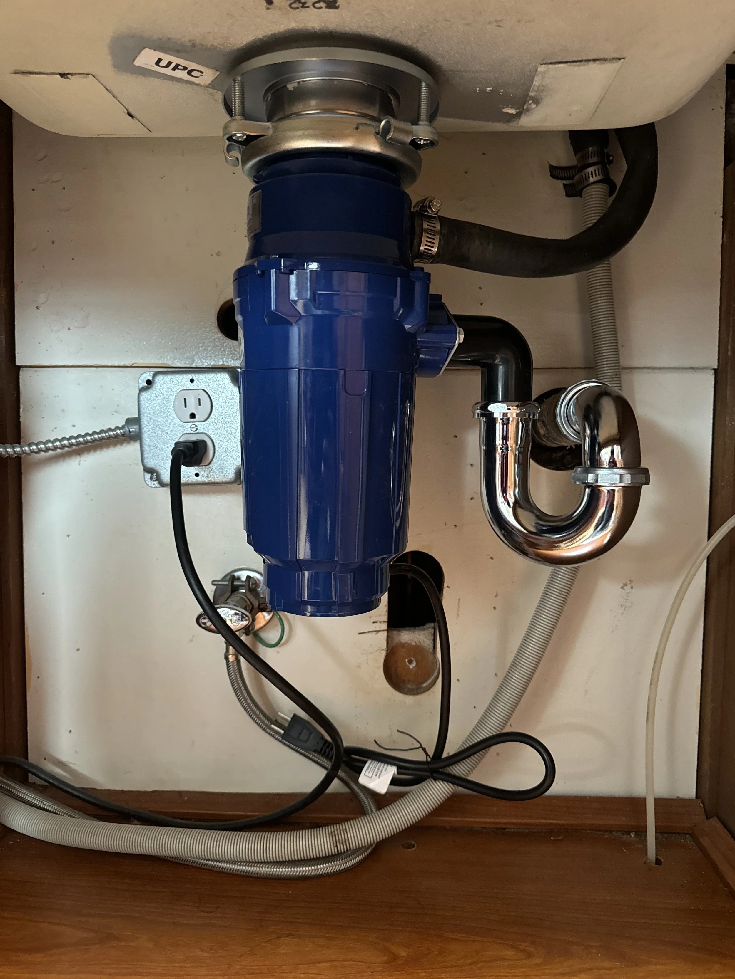 Under-sink garbage disposal unit connected to plumbing pipes and electrical outlet.