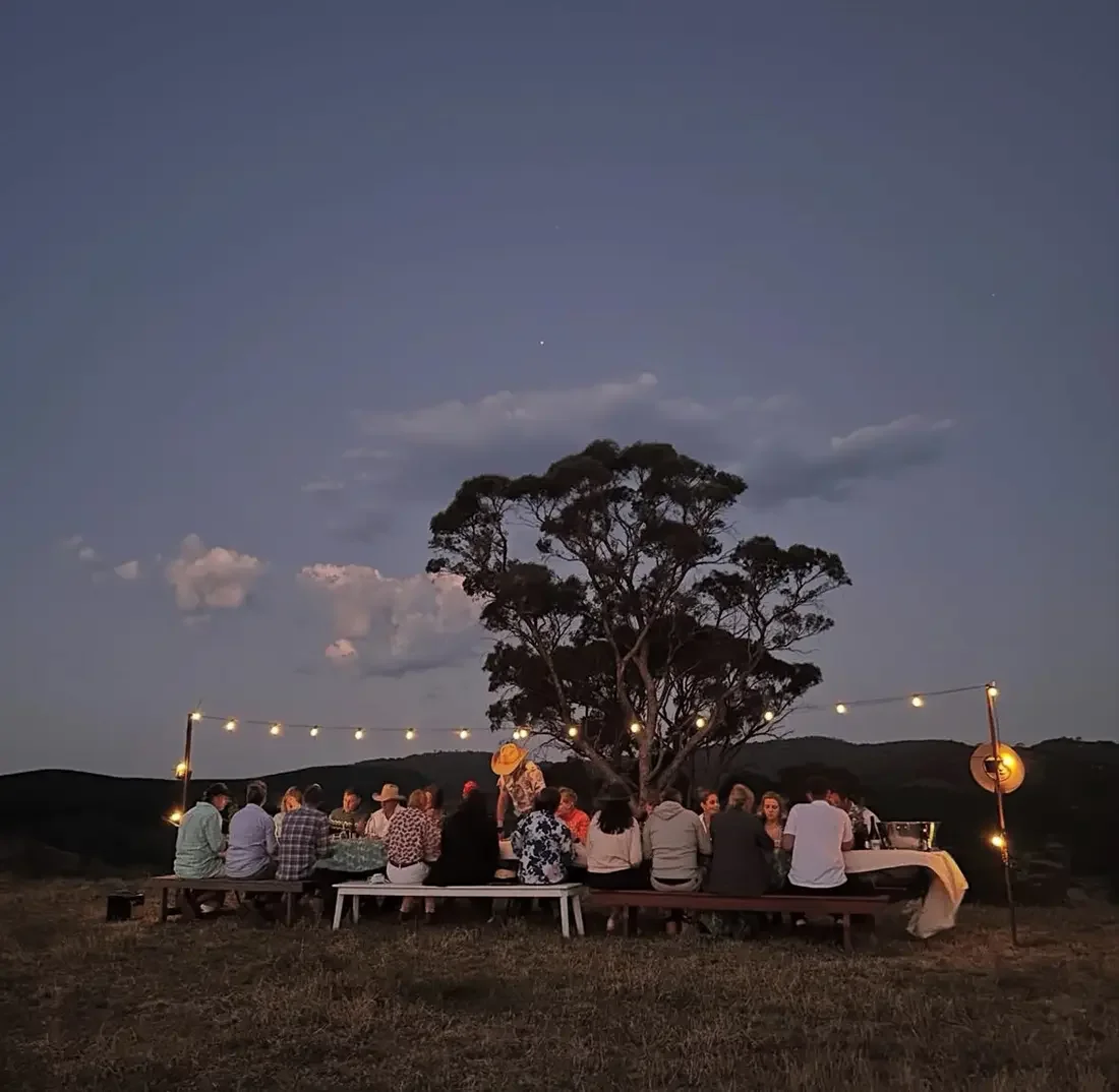 people dining outdoors at a long wooden table under the night sky