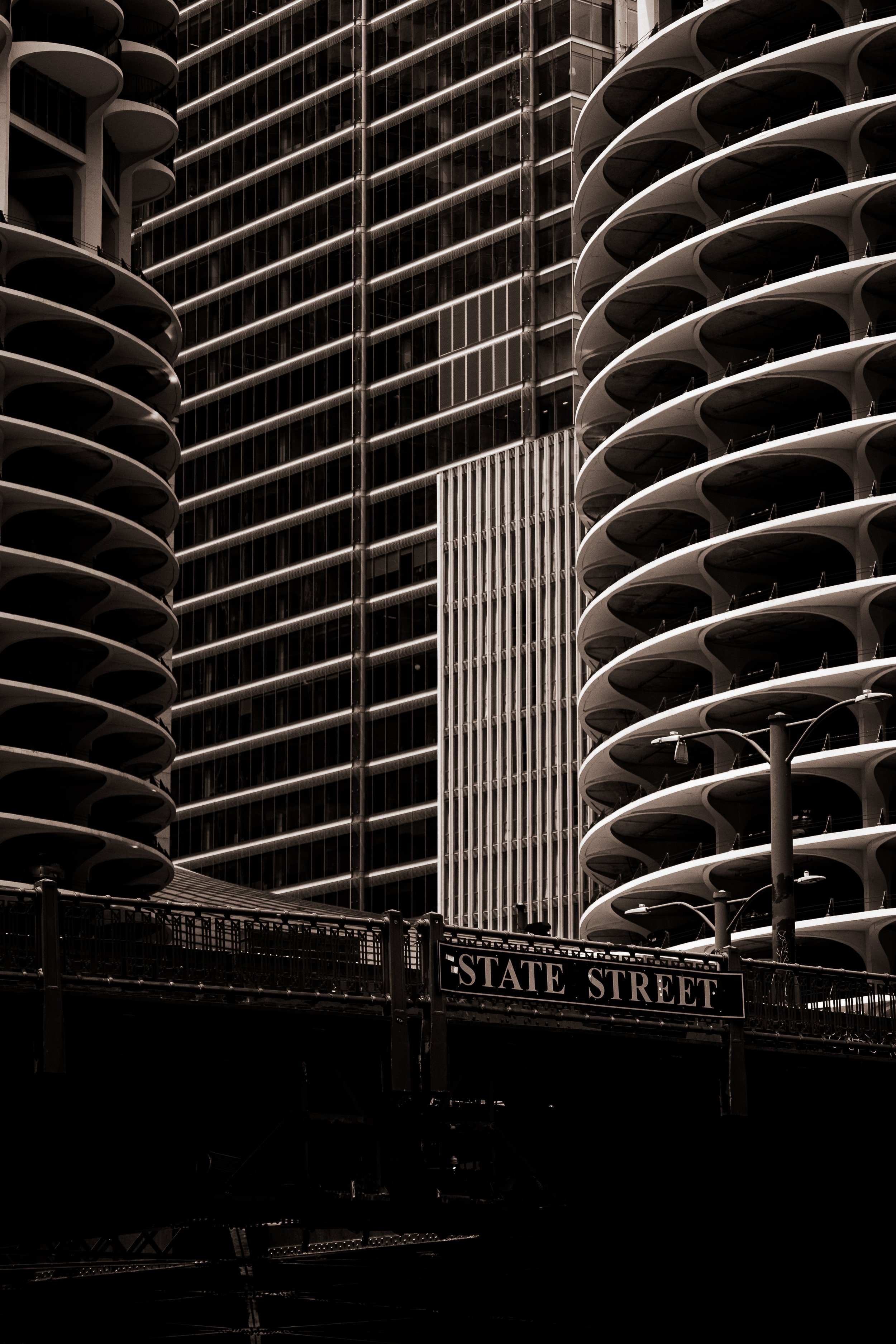 Black and white photo of modern high-rise buildings with rounded balconies and a street sign reading 'State Street' in front.