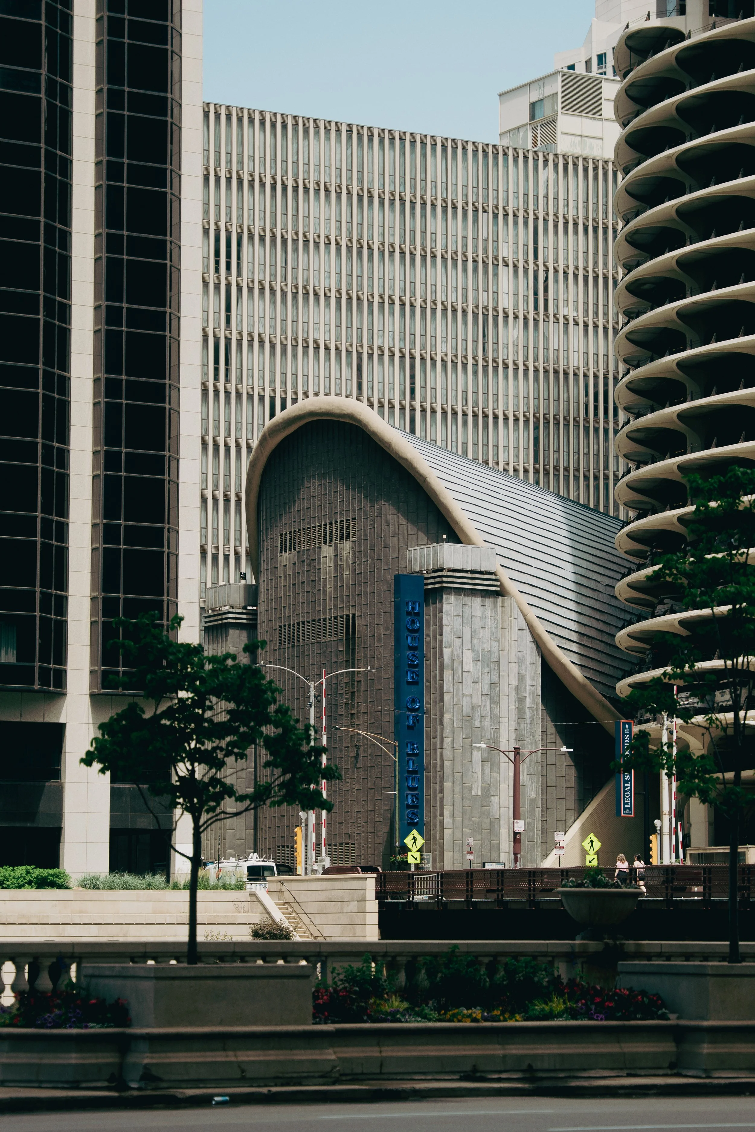 Modern cityscape featuring tall buildings, including the Museum of Modern Art with a unique wave-shaped roof, trees, and a street scene.