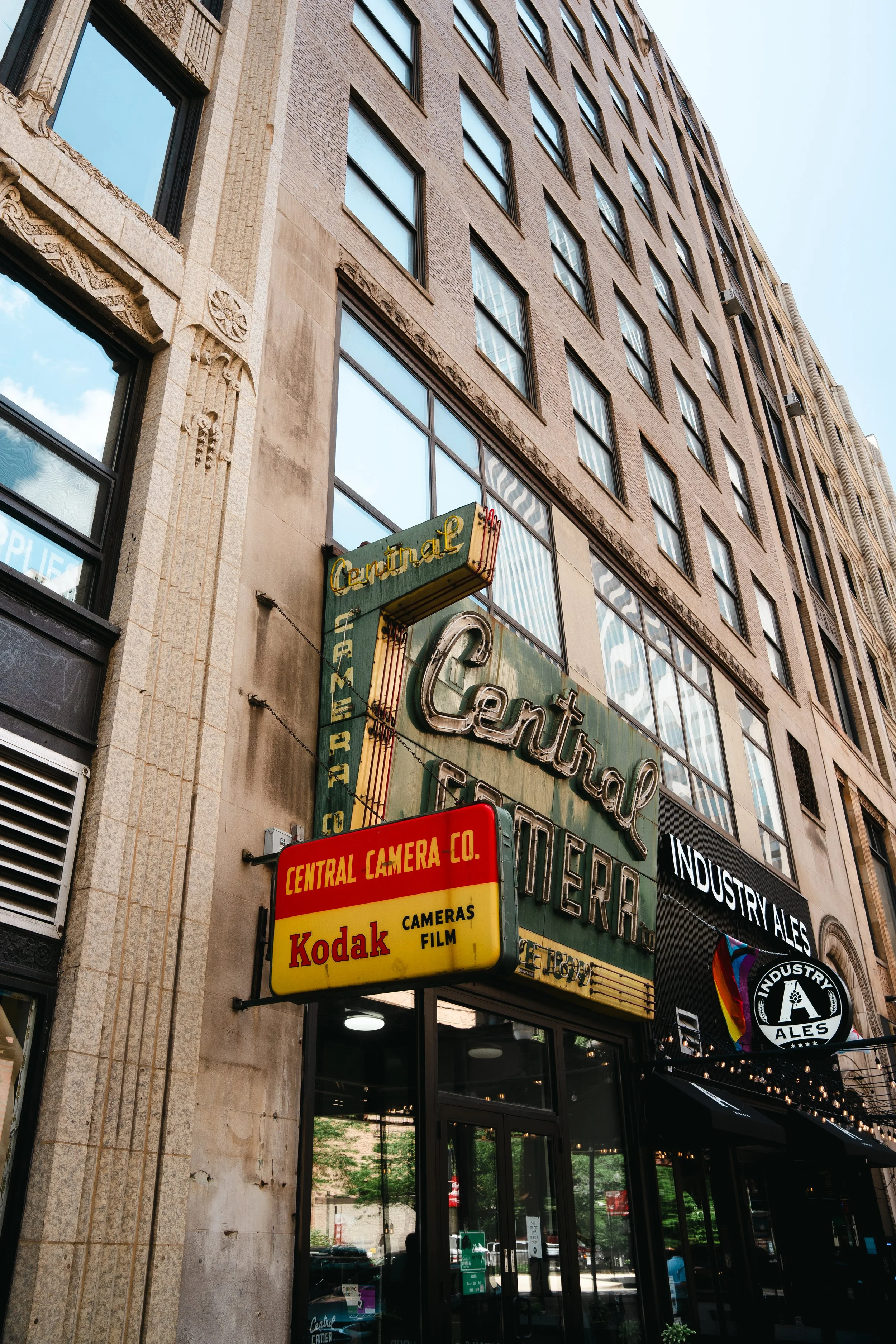 Vintage neon signs for Central Camera Store and Kodak on the side of a tall building in an urban area.