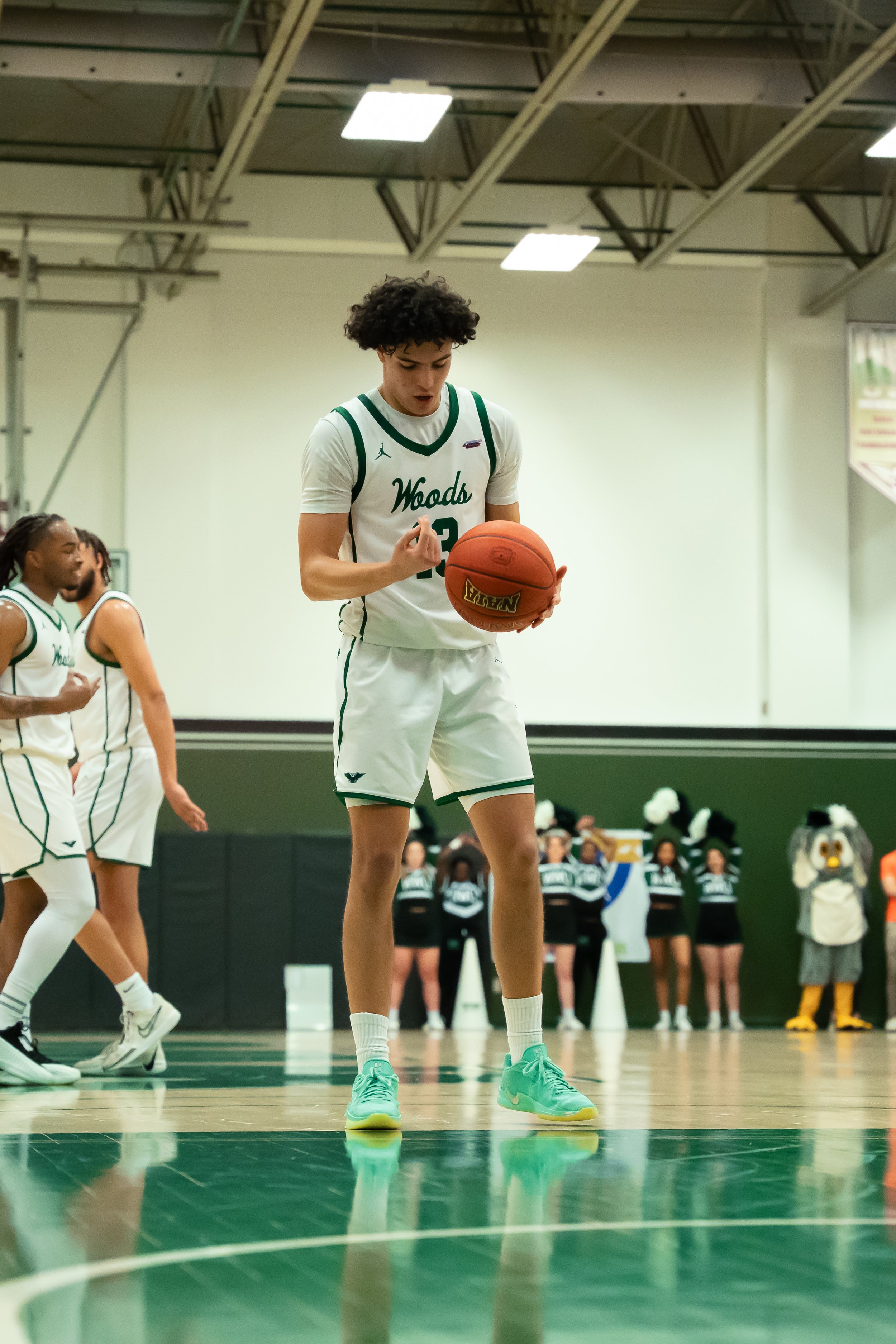 Basketball player in white and green uniform holding a basketball on a basketball court.