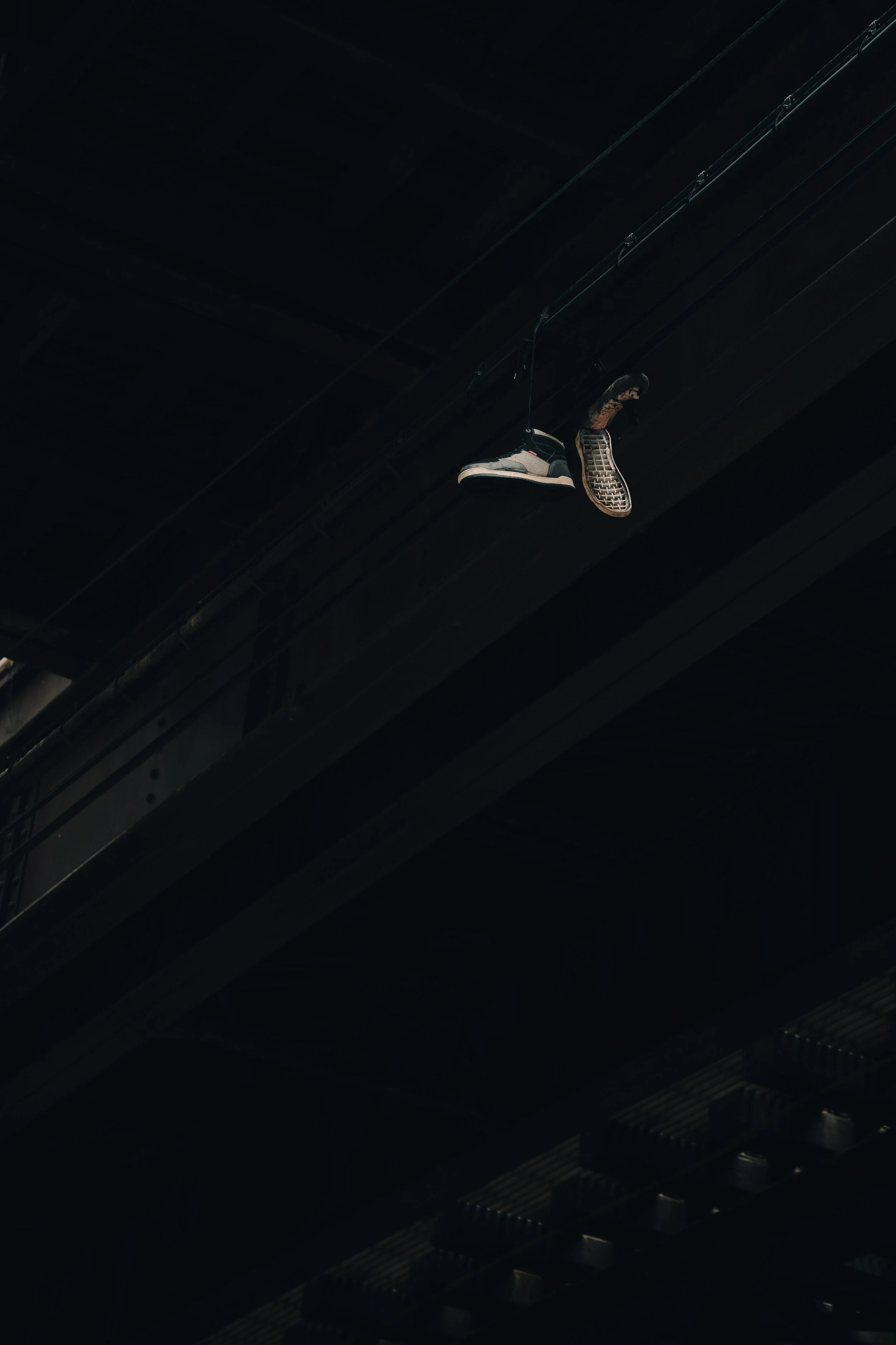Pair of sneakers hanging from a wire in a dark, industrial space.