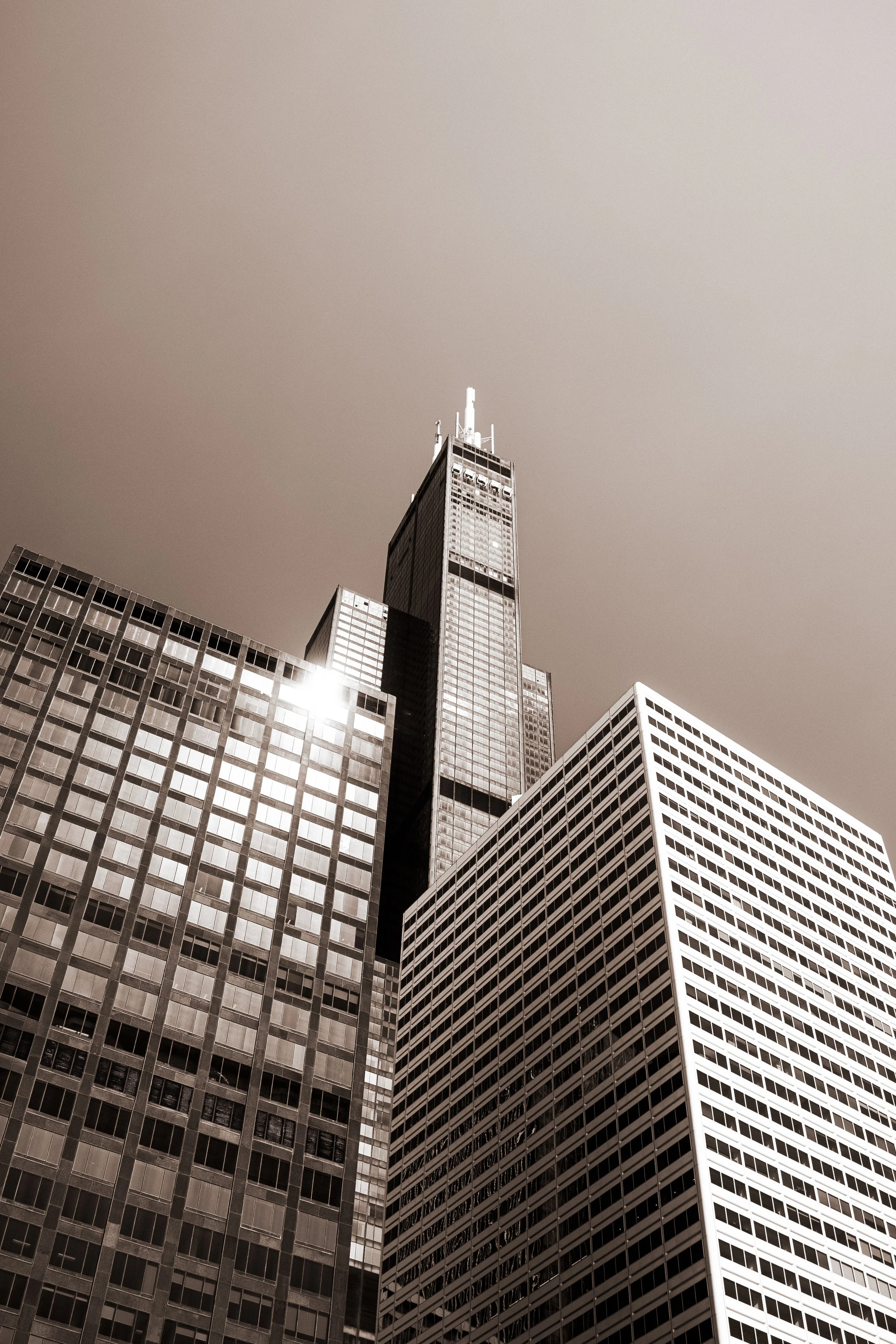 Black and white photo of tall skyscrapers, with one prominent building at the center reaching high into a clear sky.