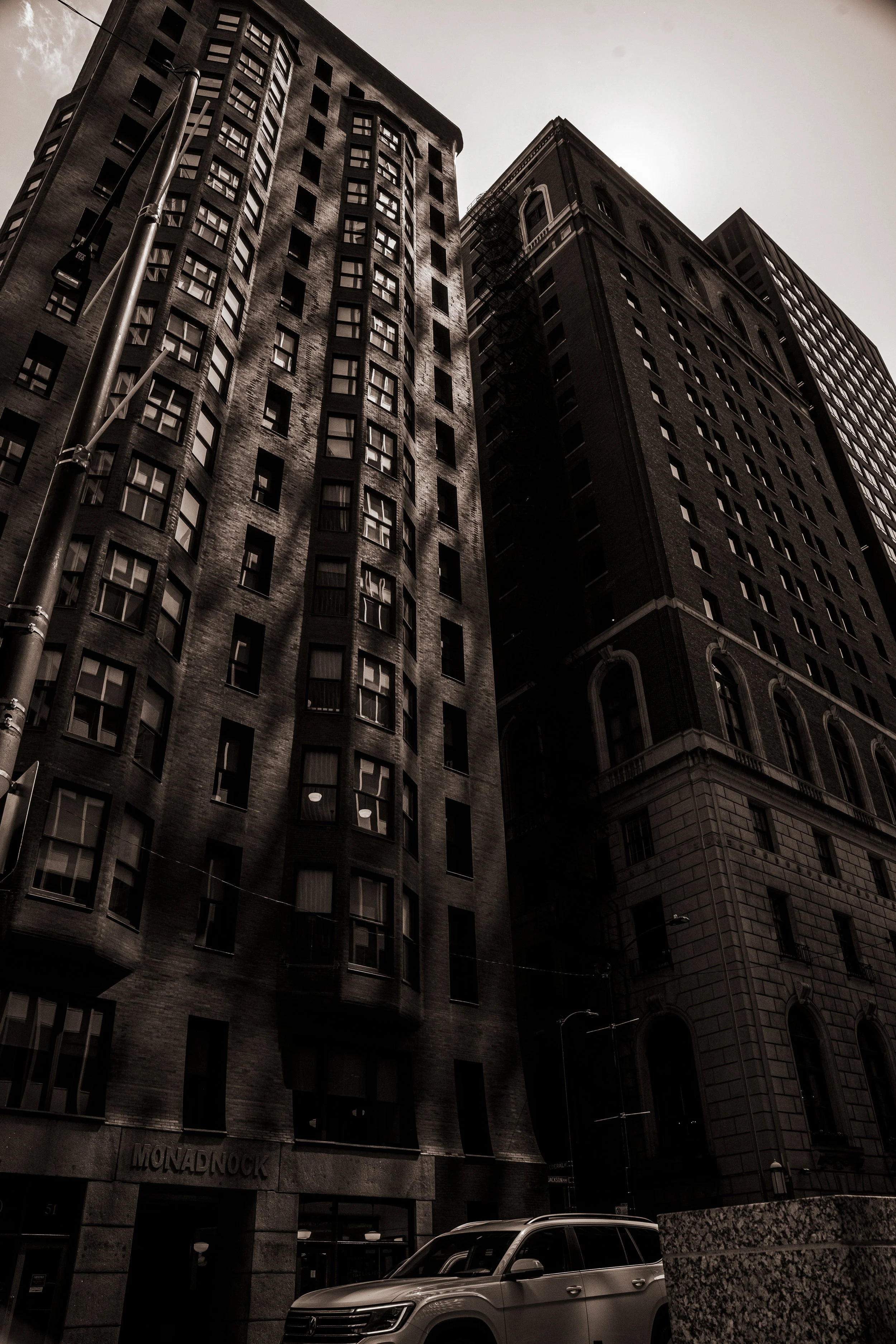 Tall dark brick apartment buildings in an urban cityscape with a car parked in front.