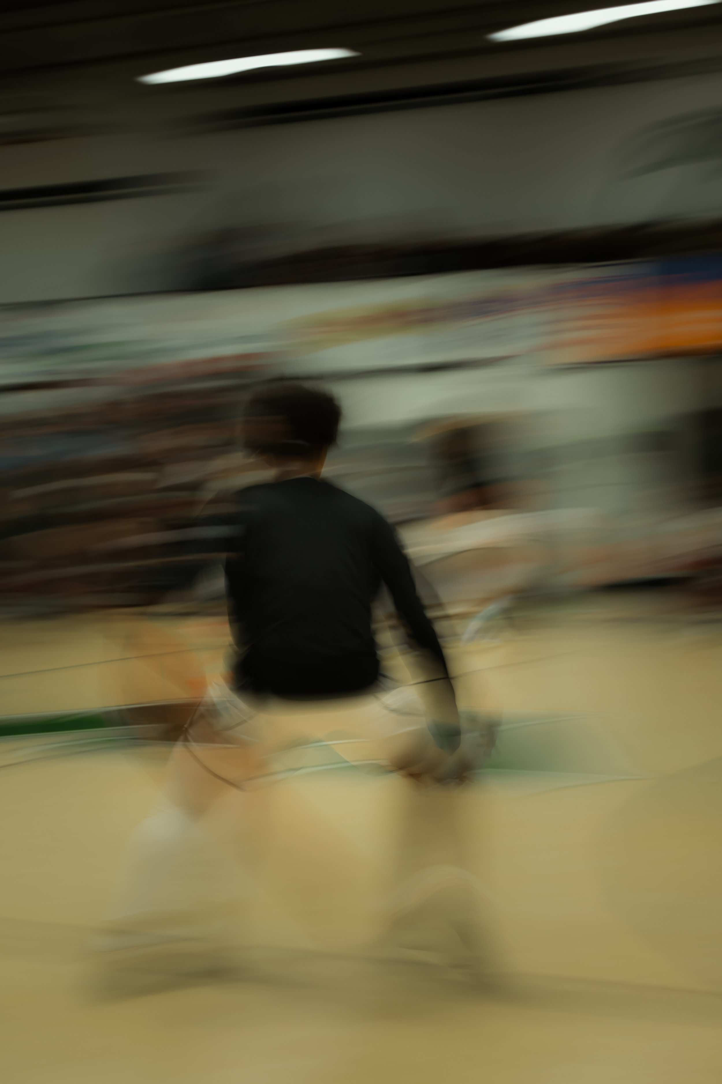 A person in black athletic clothing playing badminton indoors with a blurred background.