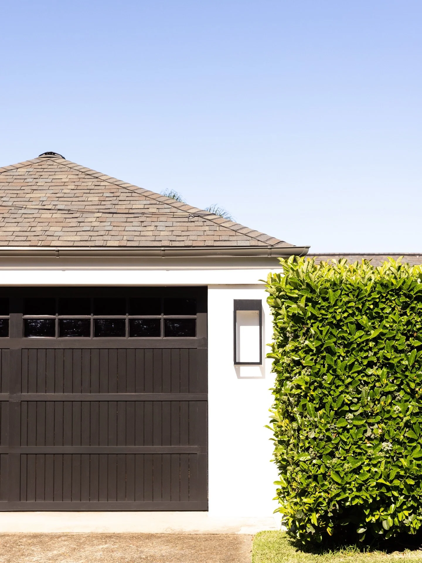 A custom timber garage door, classic white facade and a shingle roof are softened by a tailored green hedge. House design by Alex Stritt. Project @strittdesignandconstruction. Photography @simonwhitbreadphoto. #chinamansbeachhouse #strittdesignandcon