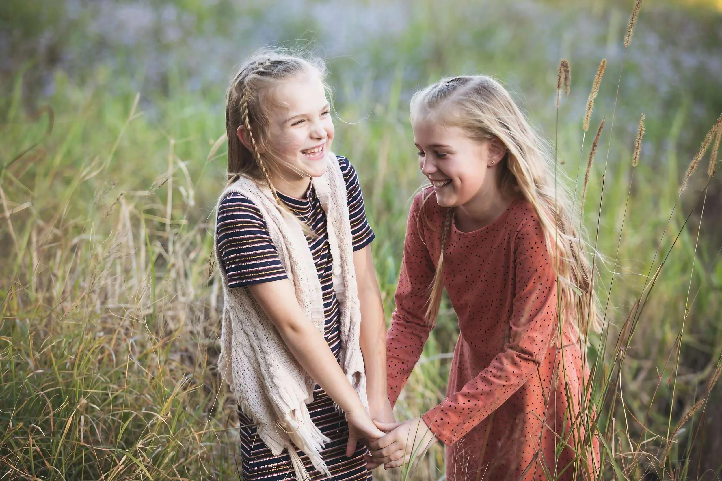 Two young girls holding hands and smiling in a grassy field.