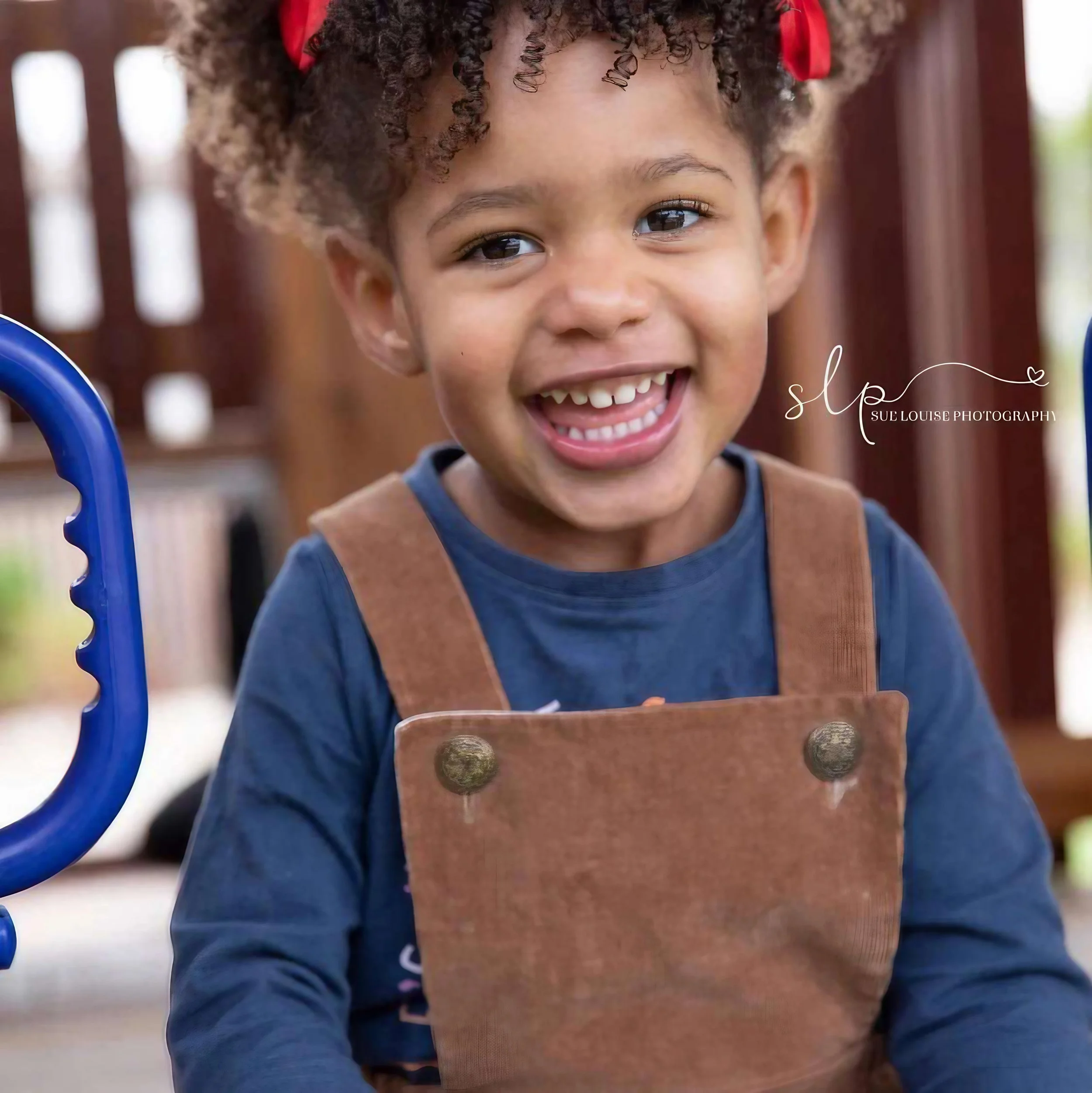 Smiling young girl with curly hair playing on a playground.