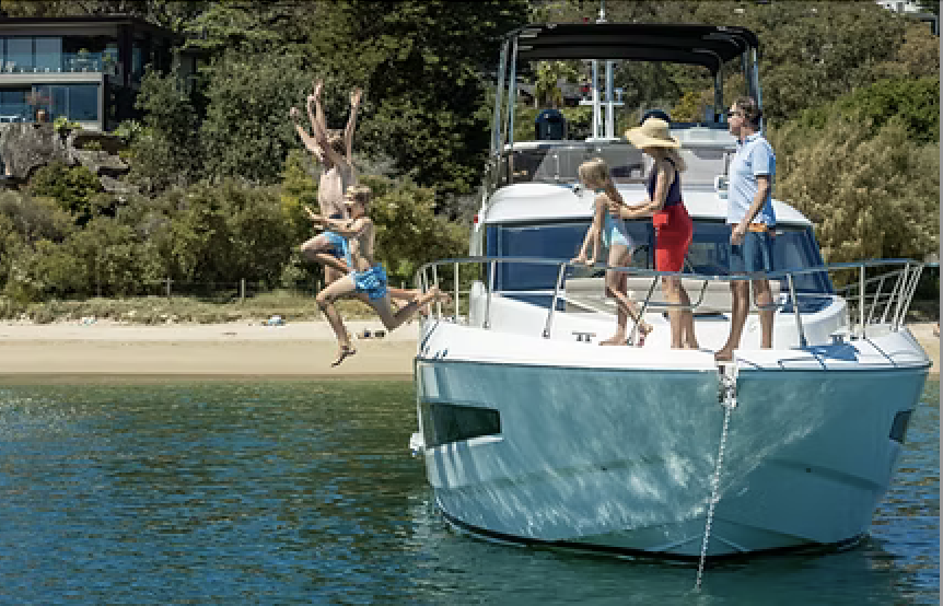 BSa - People on a boat near the water, with children jumping off into the water and two adults standing on the boat.