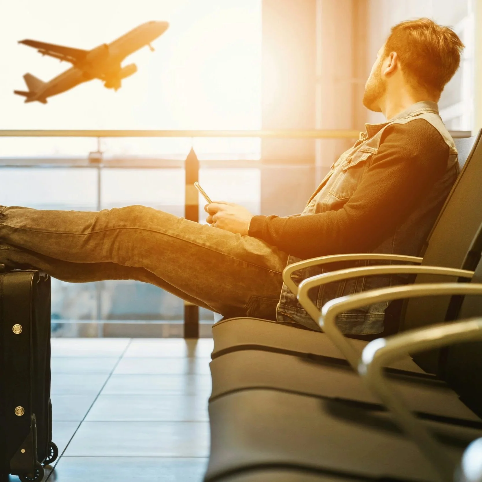 Man sitting at an airpot window watching a plane depart.