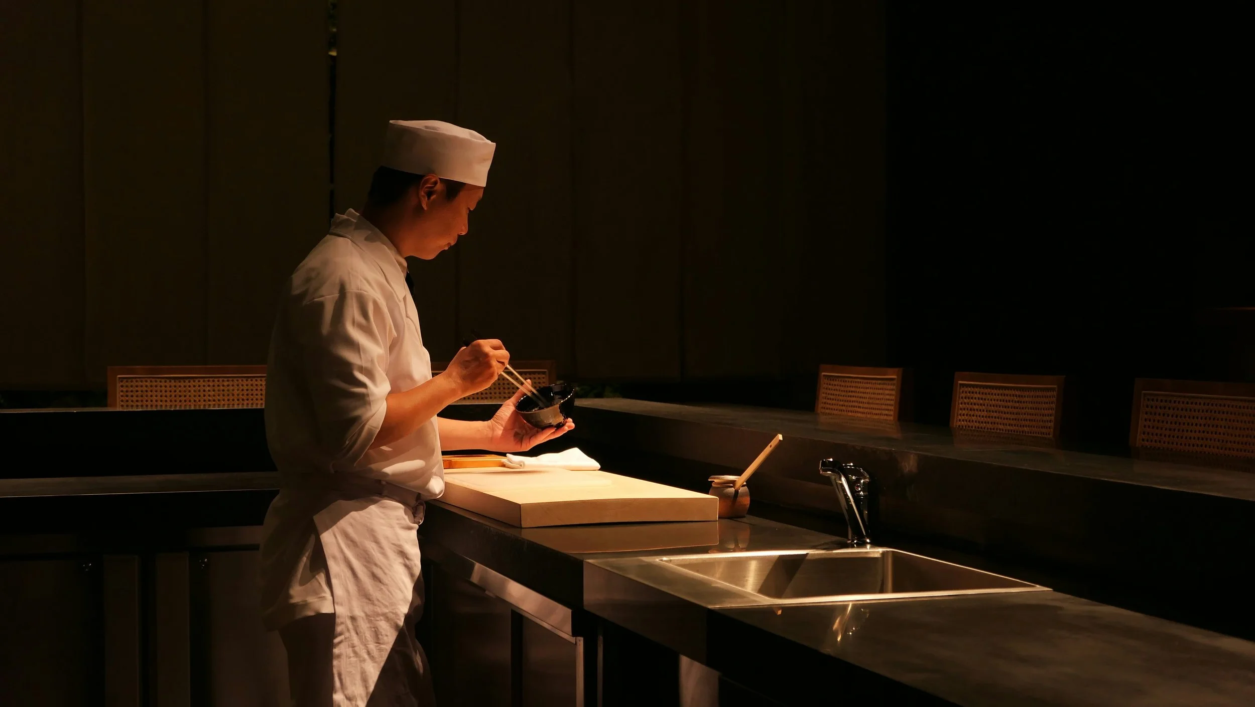 Chef using chopsticks while preparing food on a cutting board in a kitchen.