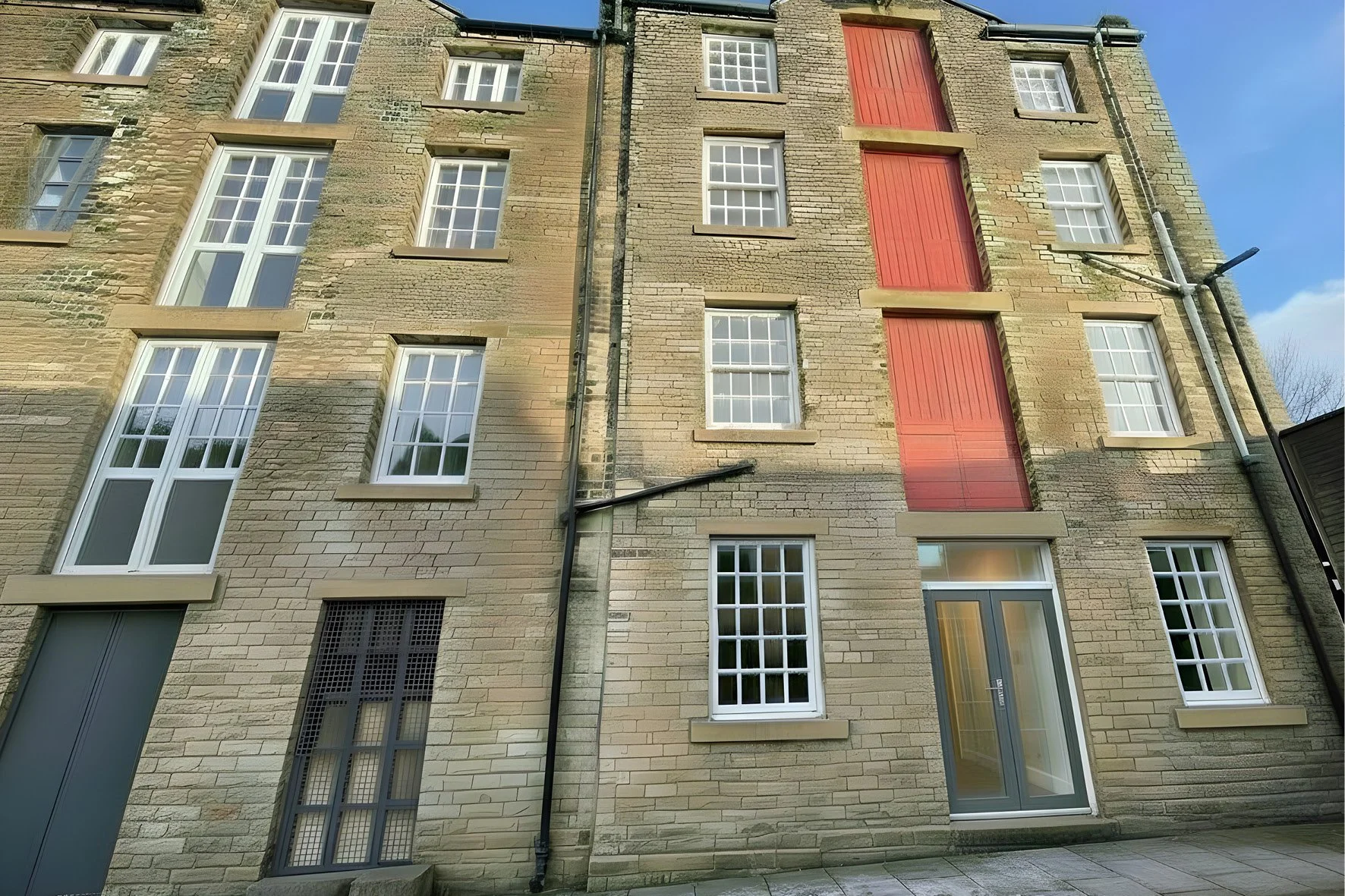 Old brick building with multiple windows and doors, some covered with shutters, and a damaged roof with missing shingles.