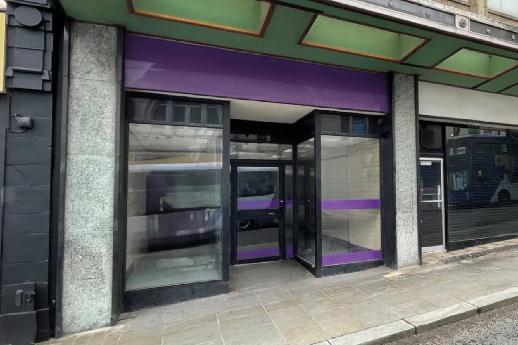 Empty store with purple accents, glass doors, and sidewalk outside, located in an urban area.