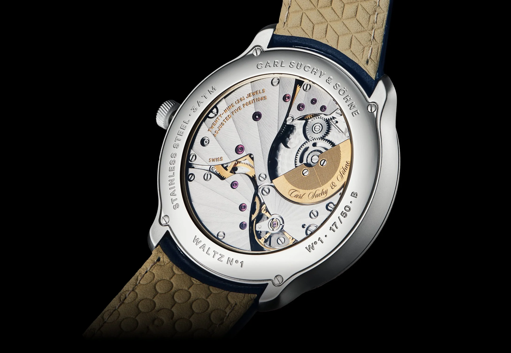 Close-up of a Waltz Nº1 with a visible mechanical movement, engraved text, and a tan textured strap, against a black background.