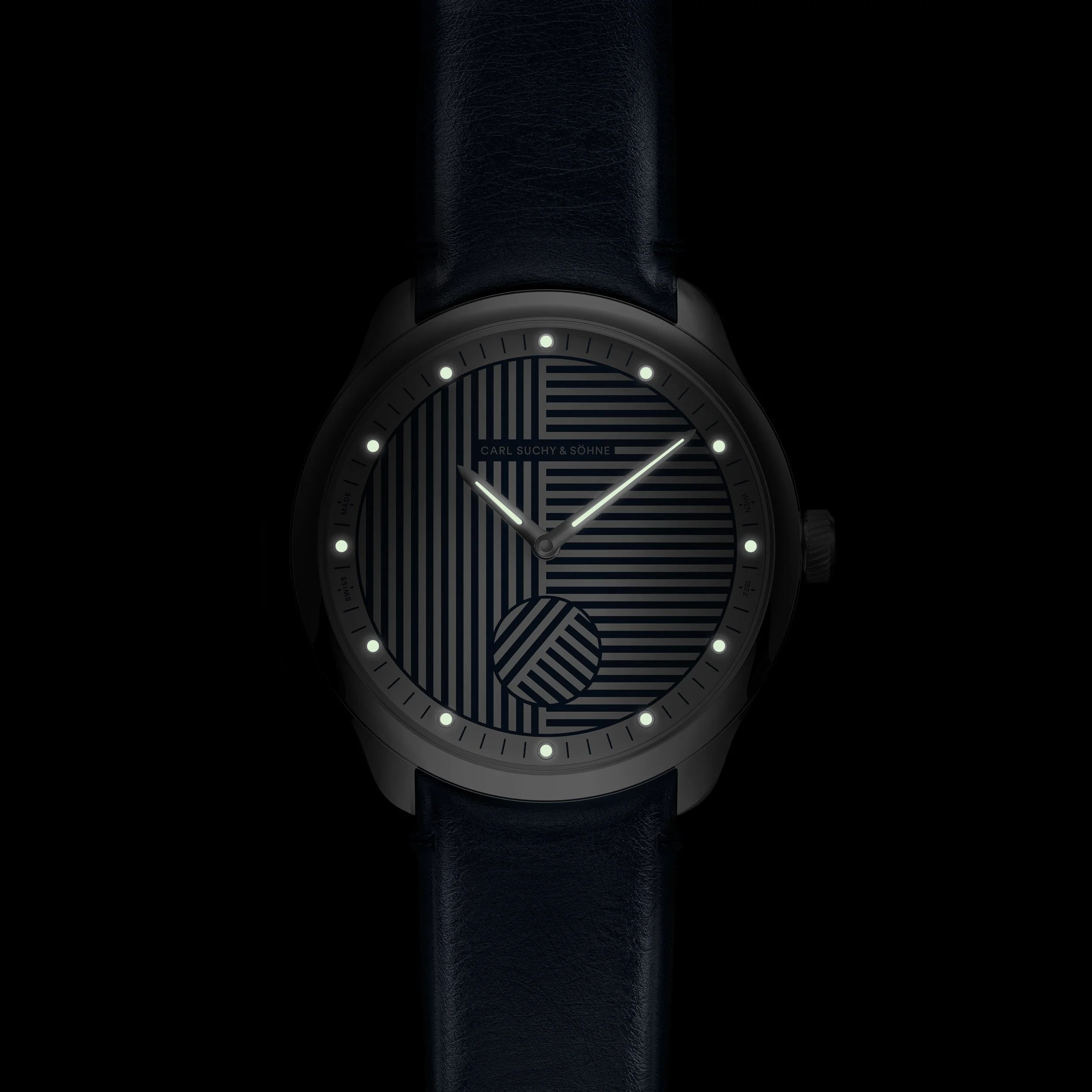 A black wristwatch with a geometric patterned dial and white luminous hour markers and hands, attached to a dark leather strap.