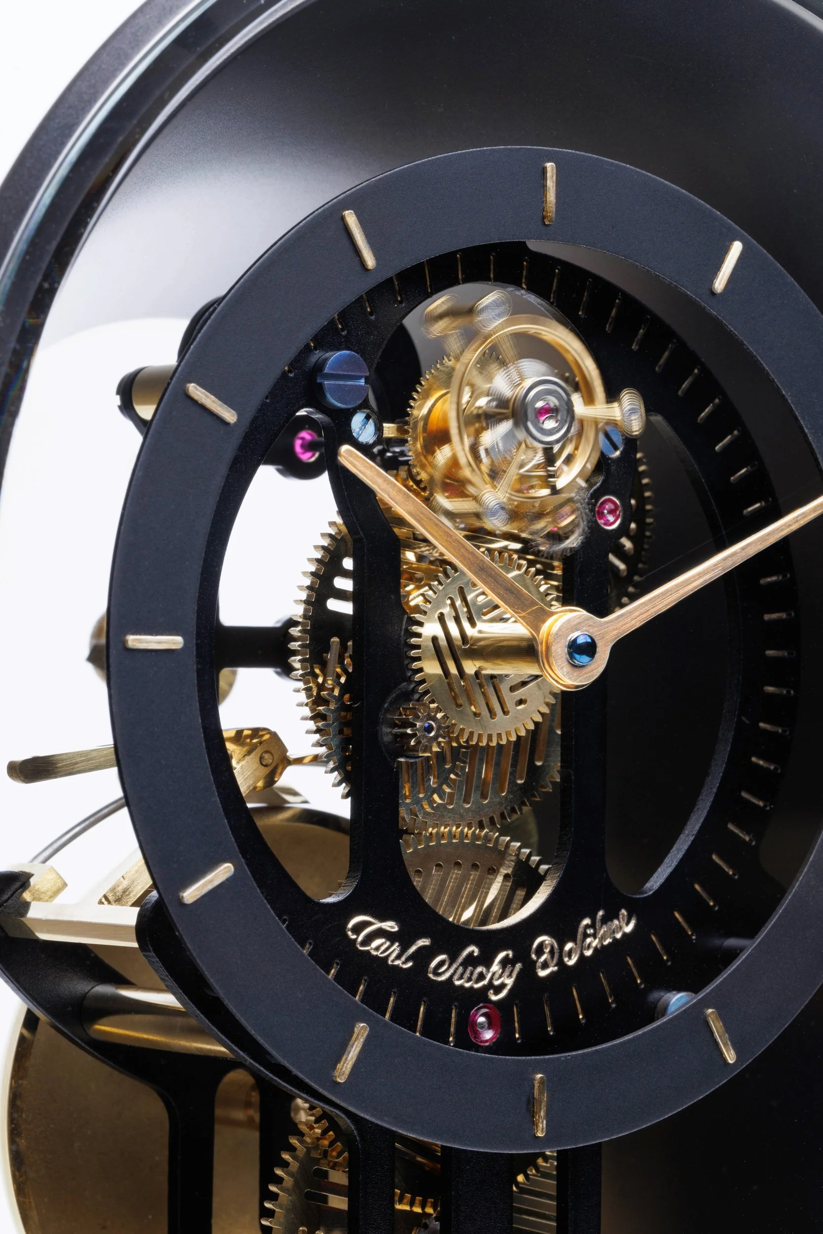 Close-up view of a mechanical clock with visible gears and intricate inner workings, including a visible balance wheel and escapement mechanism, with the signature 'Carl Suchy & Söhne' on the clock face.