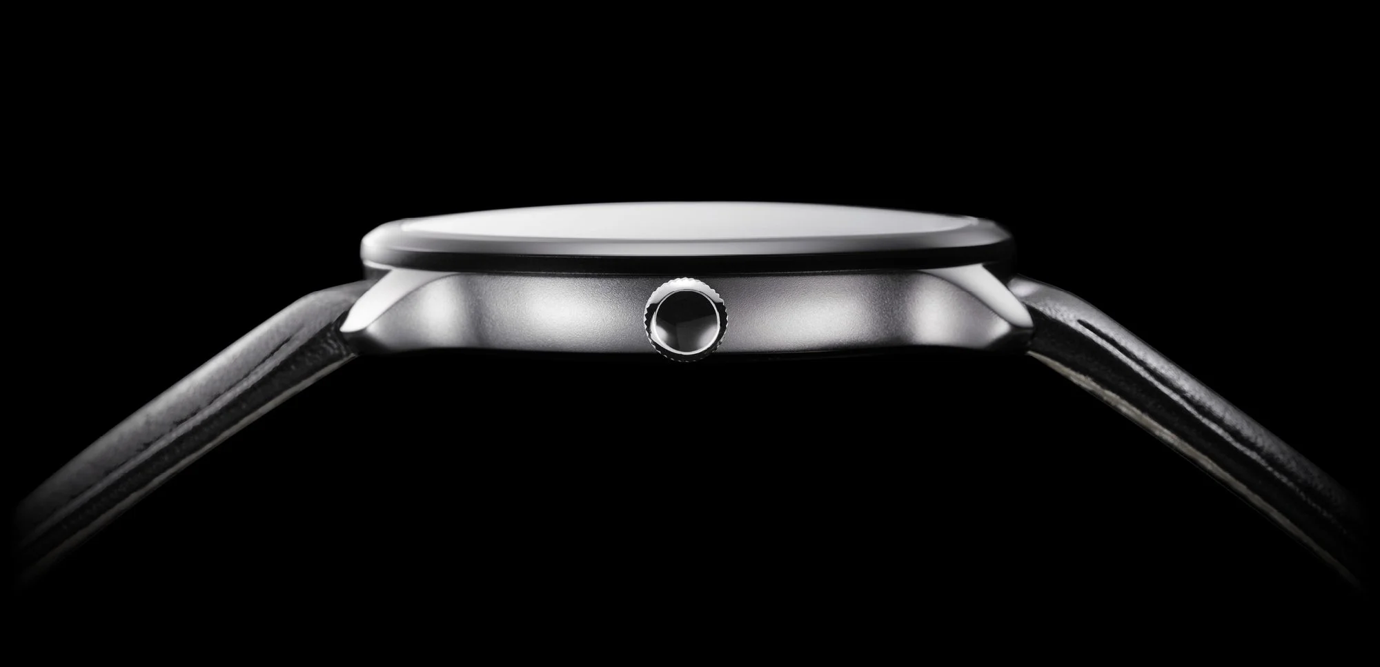 Close-up of a wristwatch with a black strap, featuring a silver case and crown, set against a black background.