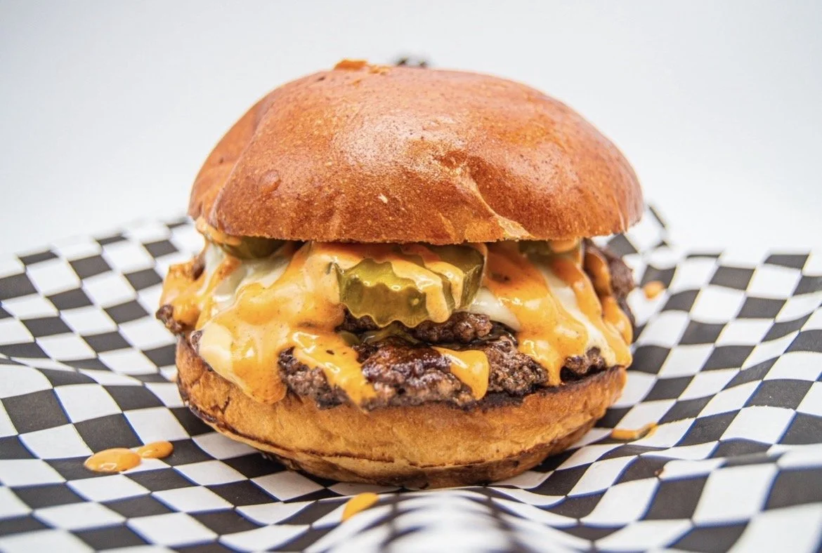 A cheeseburger with pickles in a bun on checkered paper