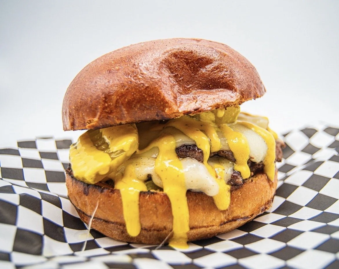 Cheeseburger with pickles, cheese, and yellow mustard in a bun on checkered paper