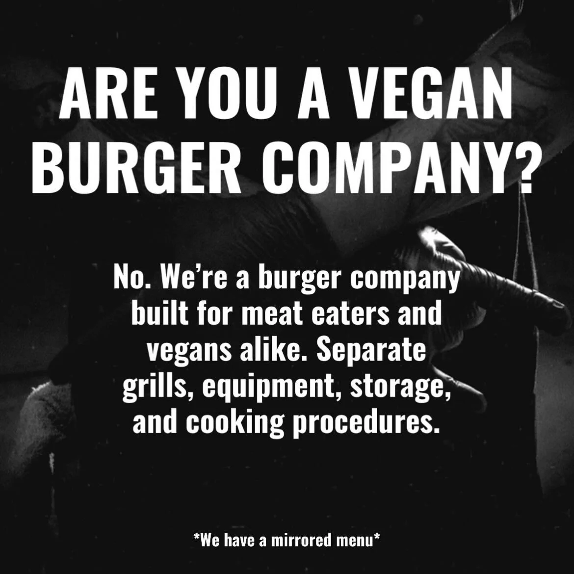 Black and white sign with bold text asking if you are a vegan burger company, explaining they are a burger company for meat eaters and vegans, with details about separate grills and equipment, and a note about a mirrored menu.