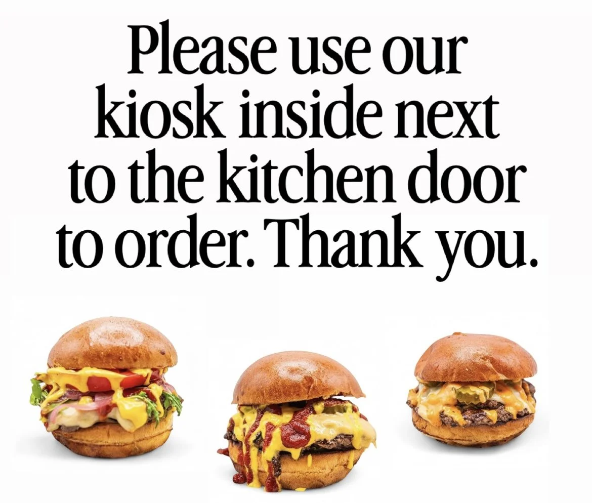 Sign instructing to use a kiosk inside next to the kitchen door, with three burgers below.