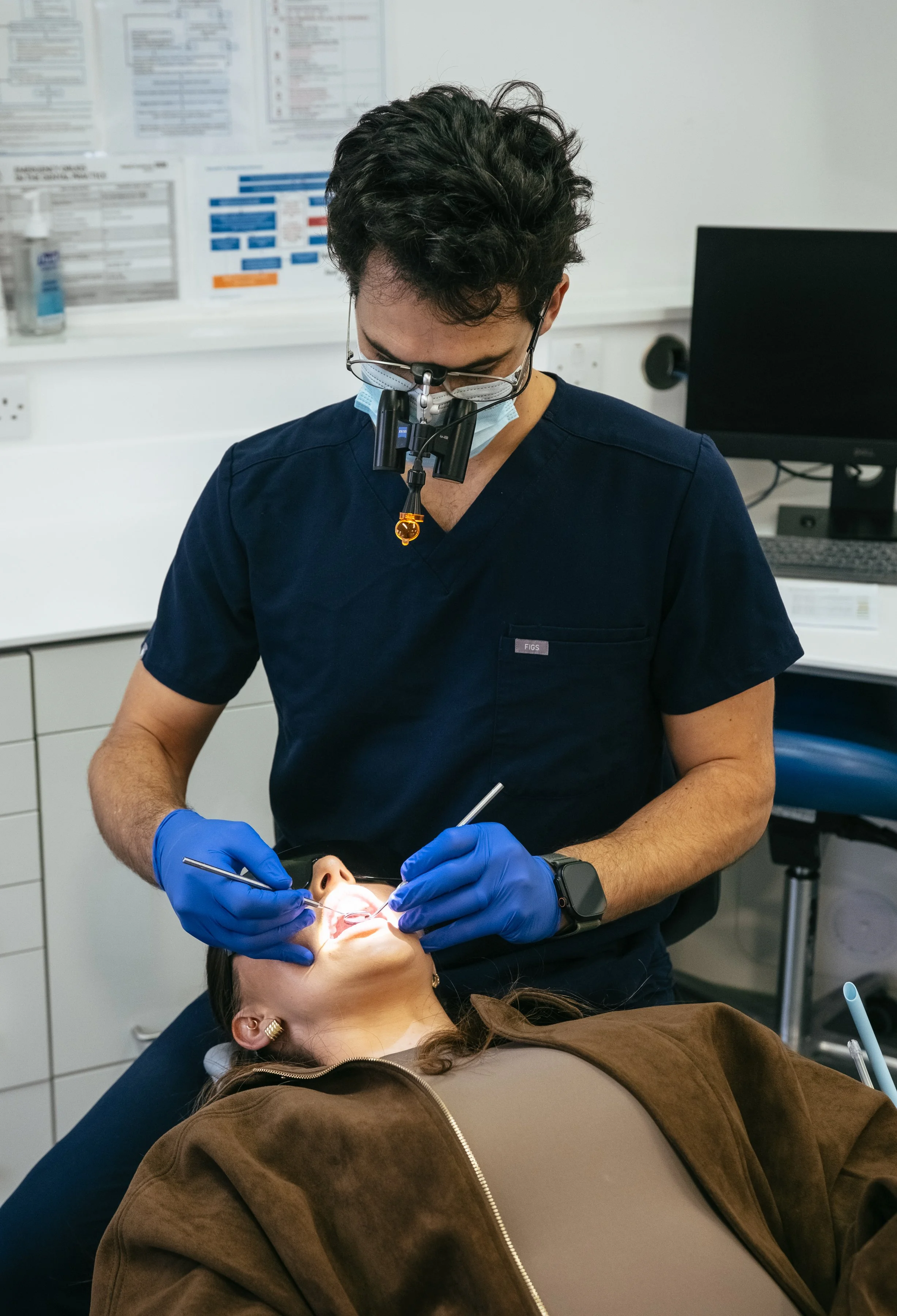 Dentist performing general dentistry using loupes and LED light while examining a patient's teeth in a modern dental clinic