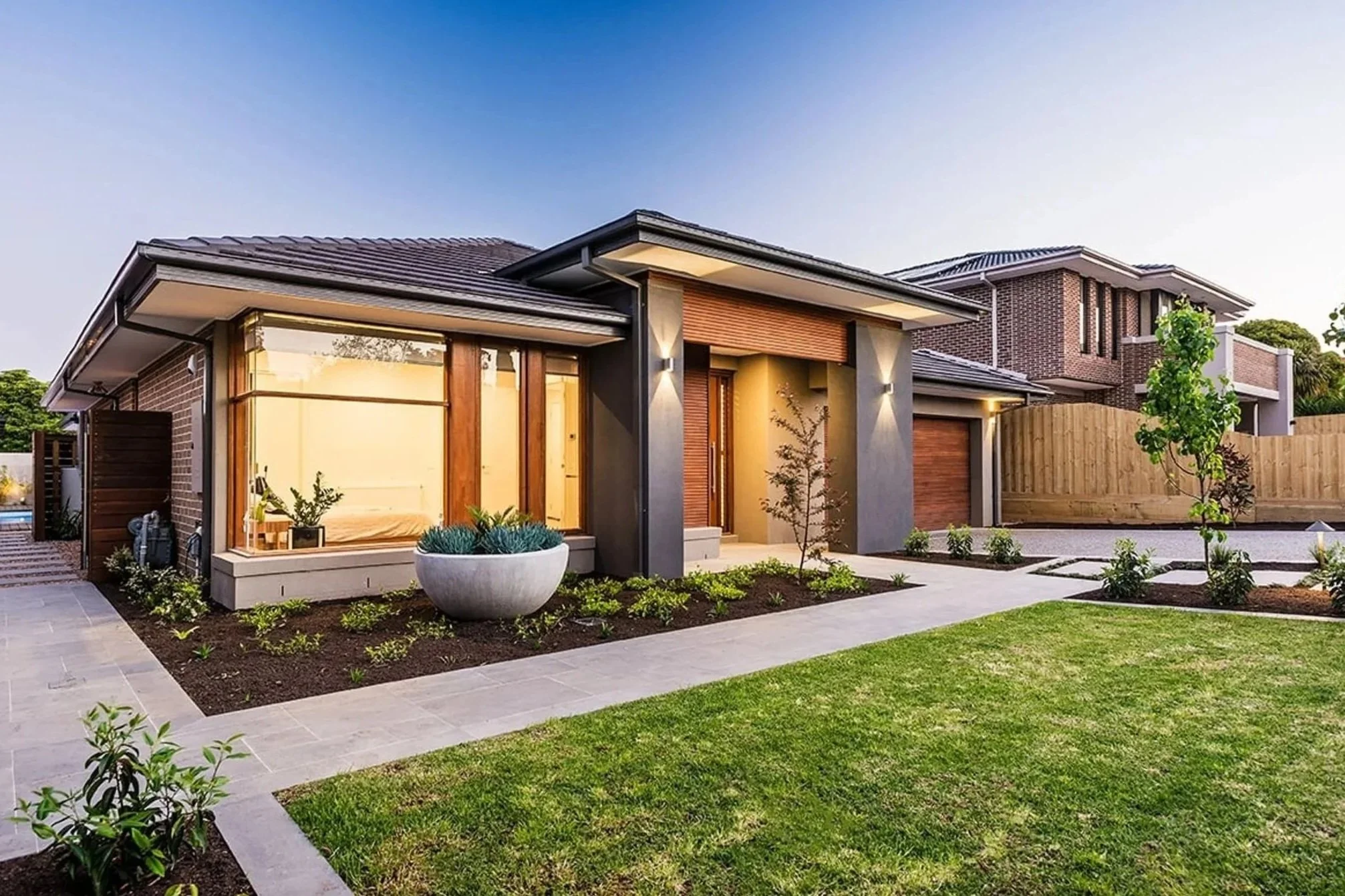 cbg construction work Modern suburban house with landscaped front yard, small trees, plants, and a pathway, under a clear sky.