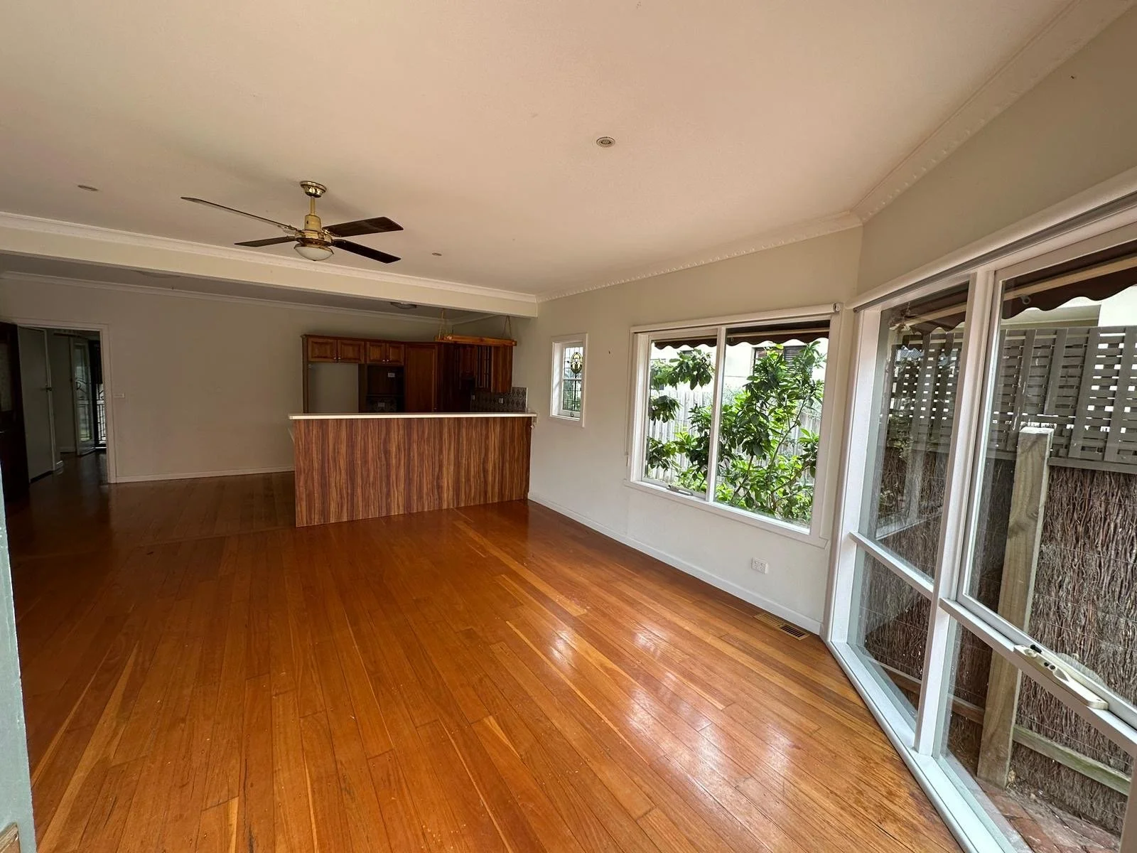 CBG CONSTRUCTION SOLUTIONS PTY LTD BEST COMPANY IN MELBOURNE Empty living room with hardwood floors, large windows, sliding glass door, ceiling fan, and a kitchen area in the background.