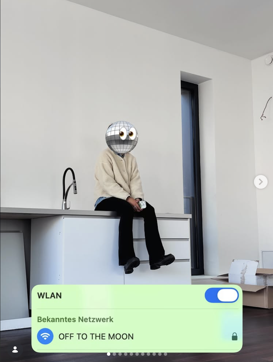 Eine Person sitzt auf einer Küchenspüle mit einem dezenten Hintergrund. Der Kopf der Person ist durch eine Diskokugelersetzt. Es gibt eine WLAN-Einstellung im Vordergrund, die auf 'OFF TO THE MOON' eingestellt ist.