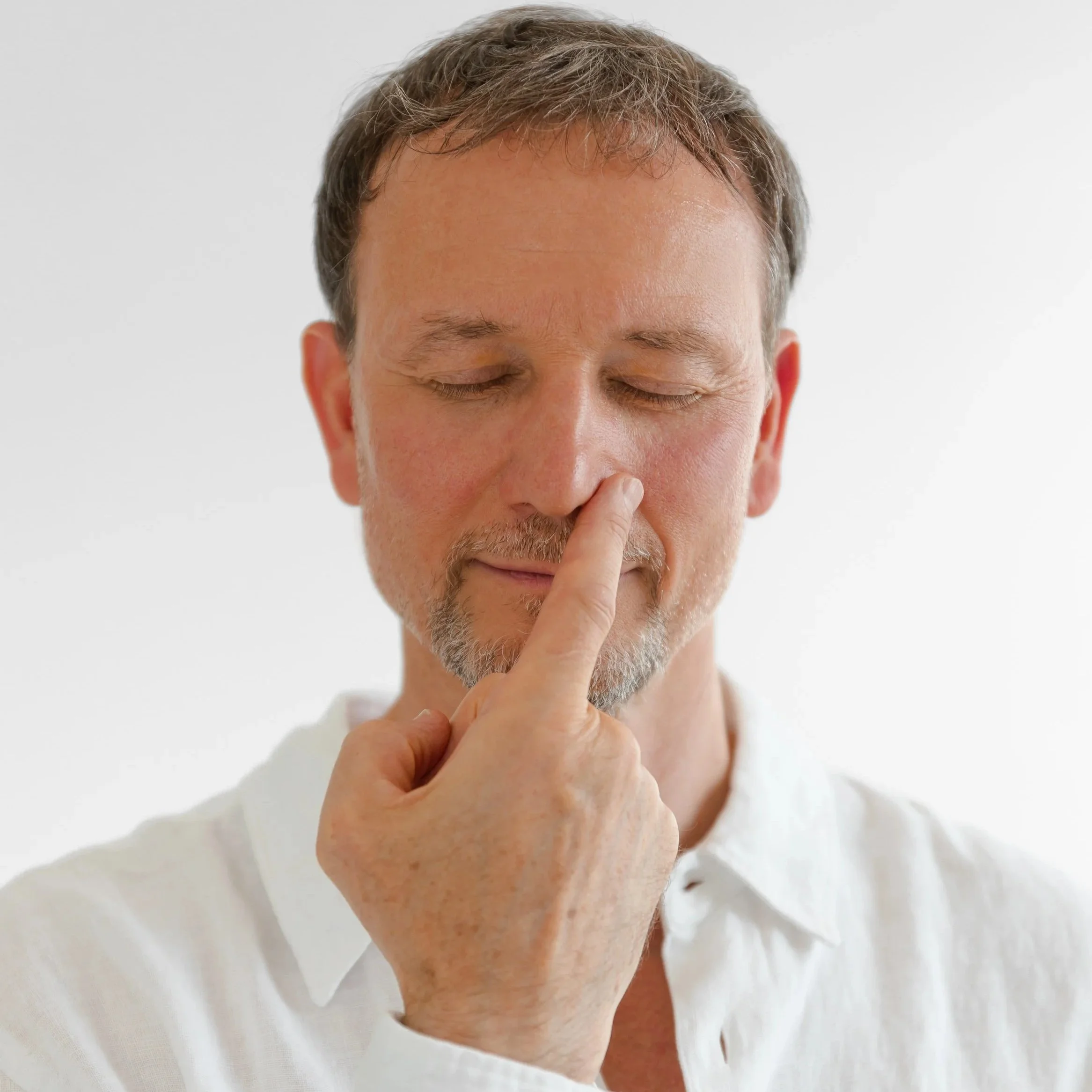 Man in white shirt with eyes closed, gently touching nose with index finger.