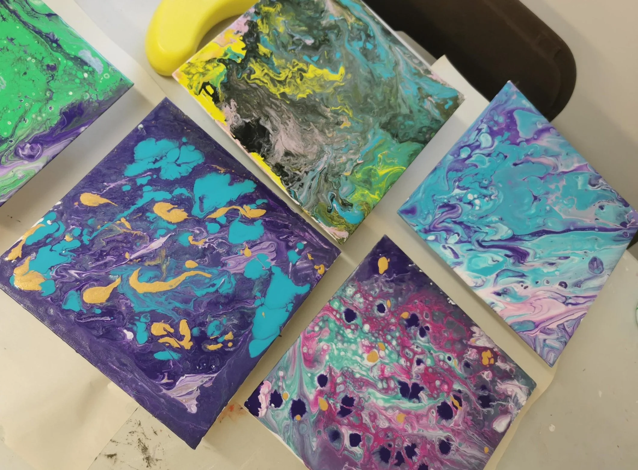Five abstract acrylic paintings with vibrant marbled swirls and splashes of color, laid out on a white table.