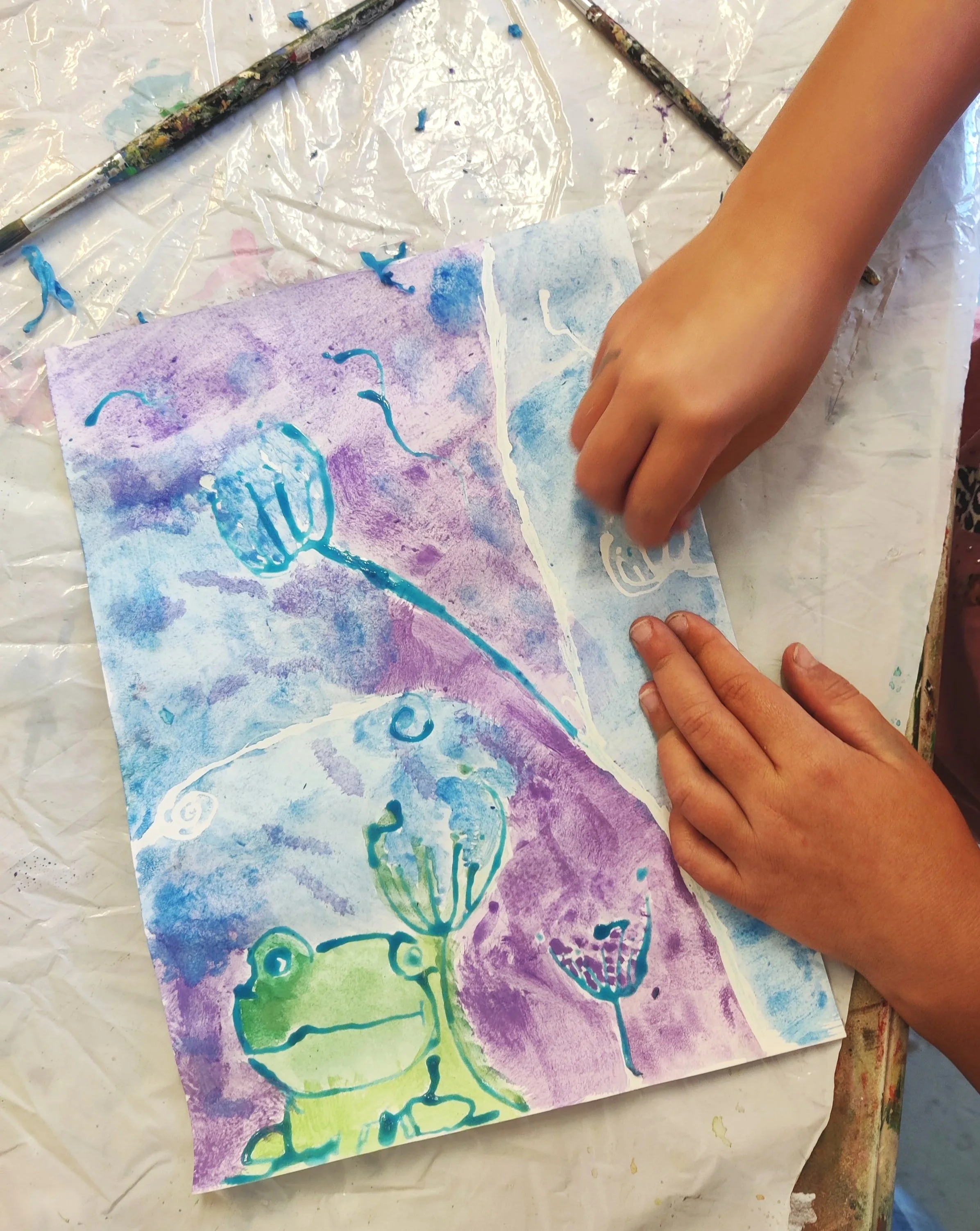 Children's watercolor painting featuring outlines of flowers in blue, green, and purple with abstract backgrounds on a piece of paper.