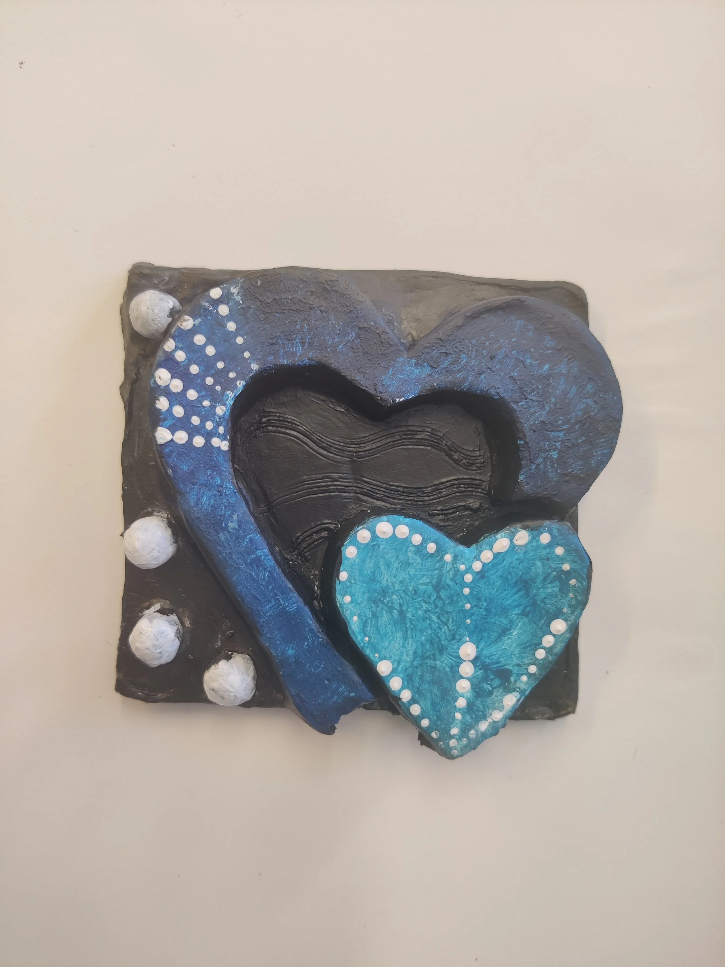 Decorative mixed media art piece with layered hearts, blue and black colors, and white dotted accents, mounted on a black square base.