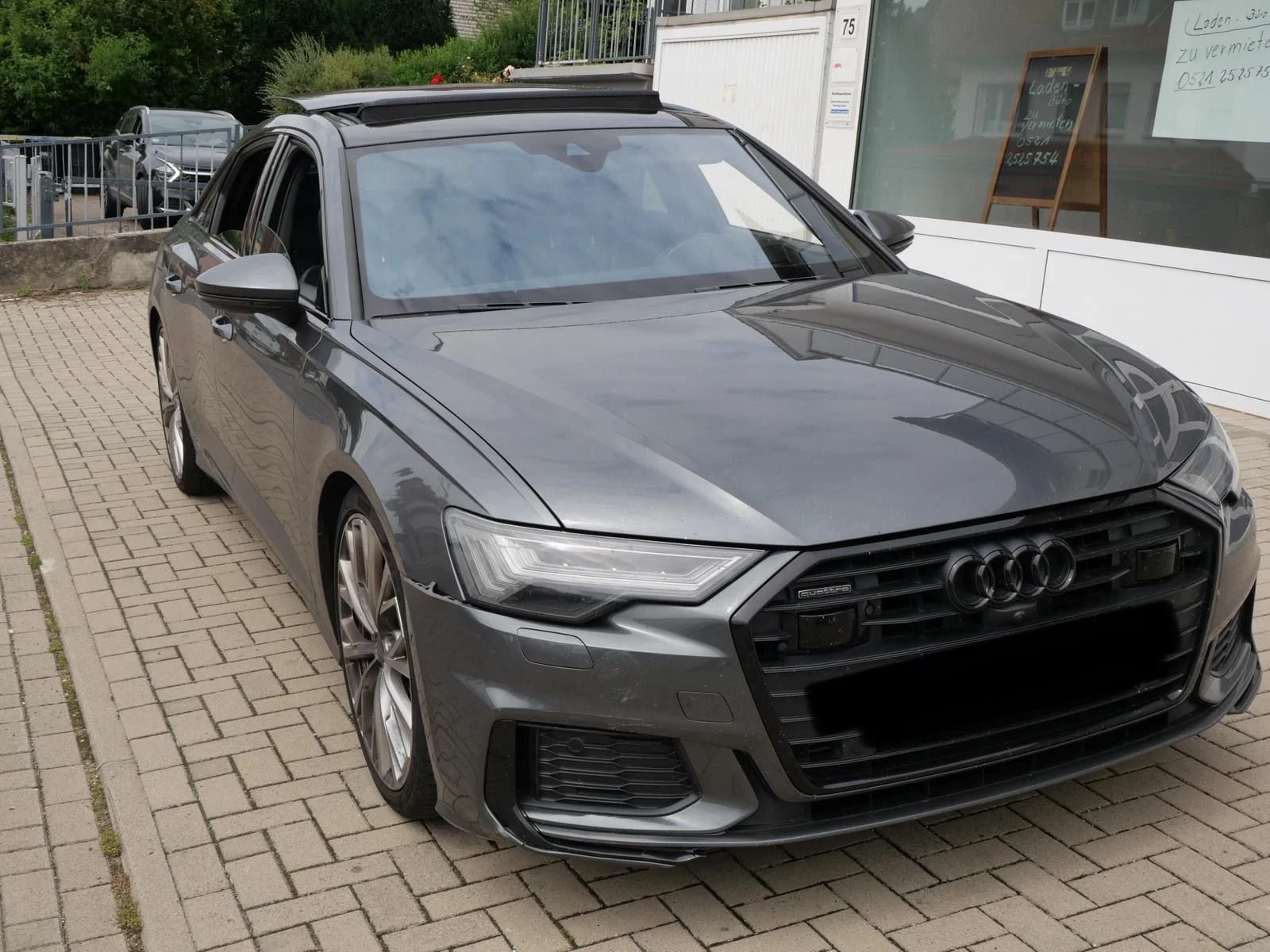 Schwarzer Audi mit großer vorderer Grillpartie, stehende auf gepflastertem Parkplatz vor einem Geschäftsgebäude.
