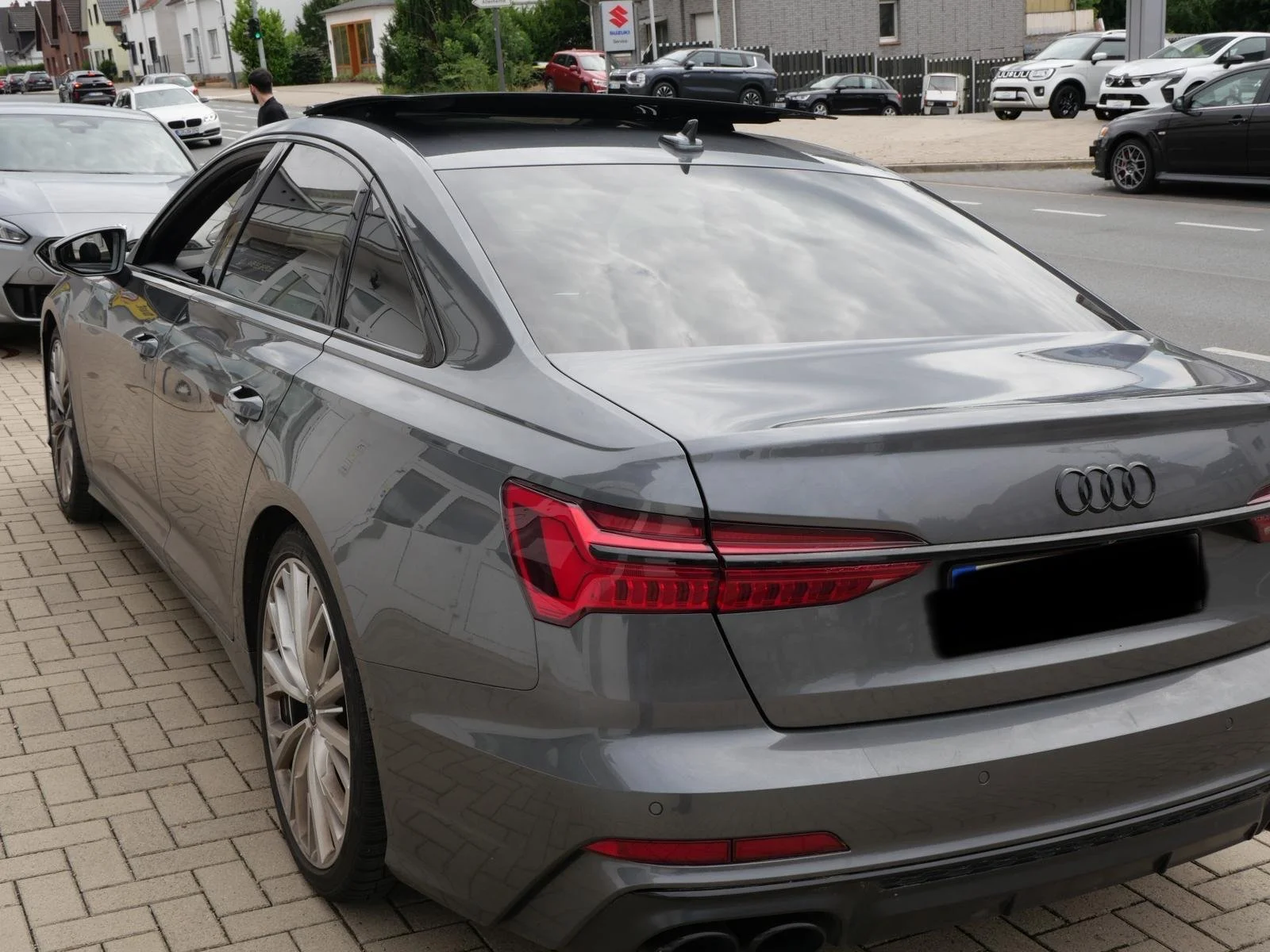 Ein grauer Audi-Auto auf einem Parkplatz, umgeben von anderen Fahrzeugen, mit einer Stadtstraße im Hintergrund.