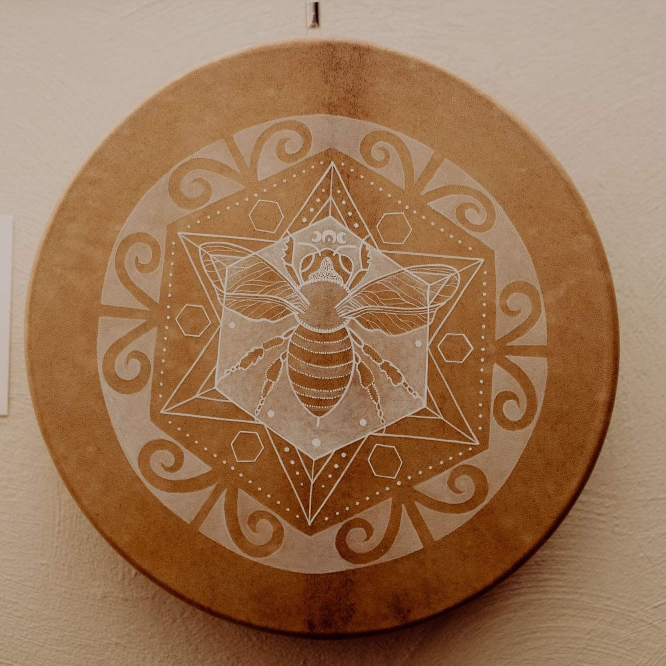 Decorative wooden drum featuring a geometric design of a bee at the centre, surrounded by hexagons and swirling patterns, with a honeycomb motif.