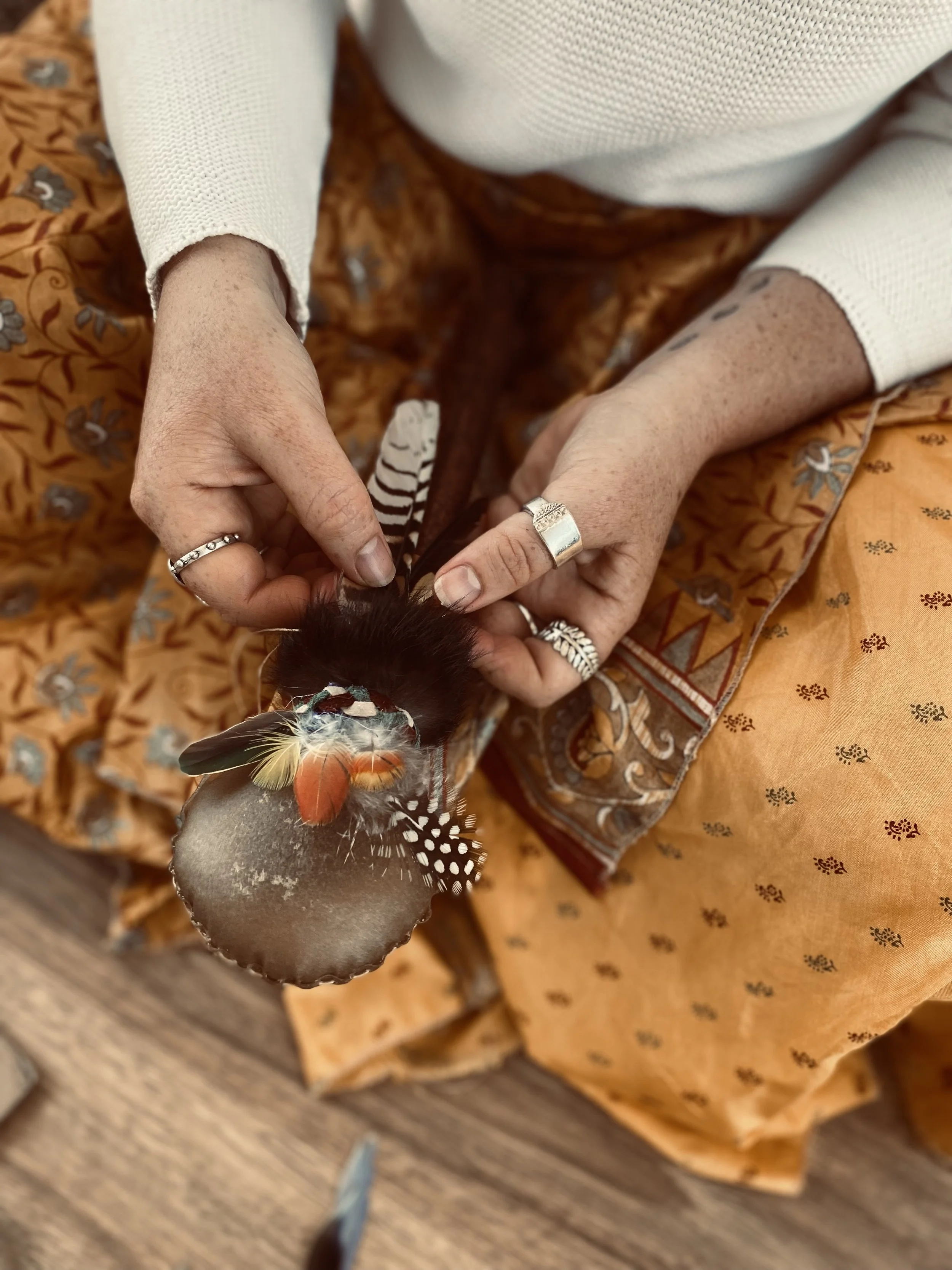 Person holding a decorated feathers-topped rattle with feathers attached.