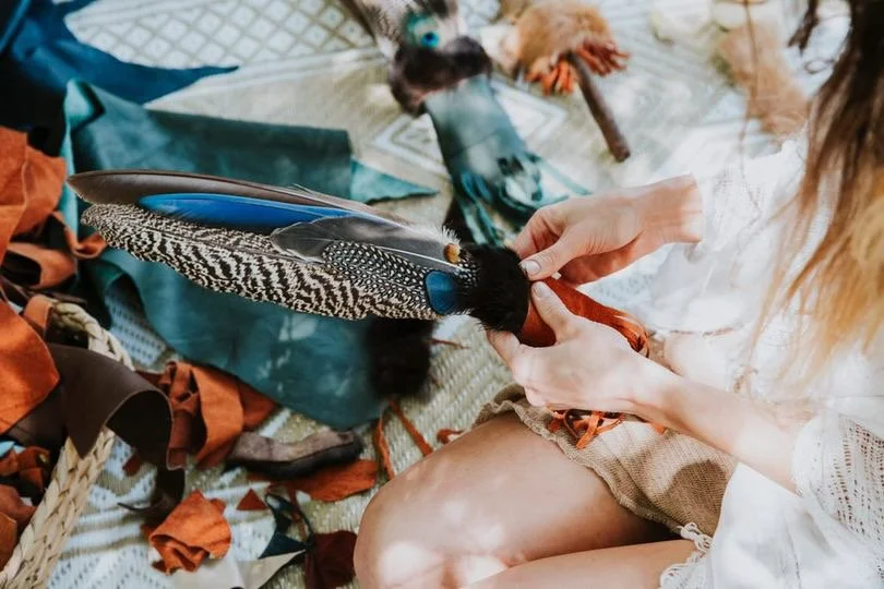 Women crafting with colourful materials and feathers around her.