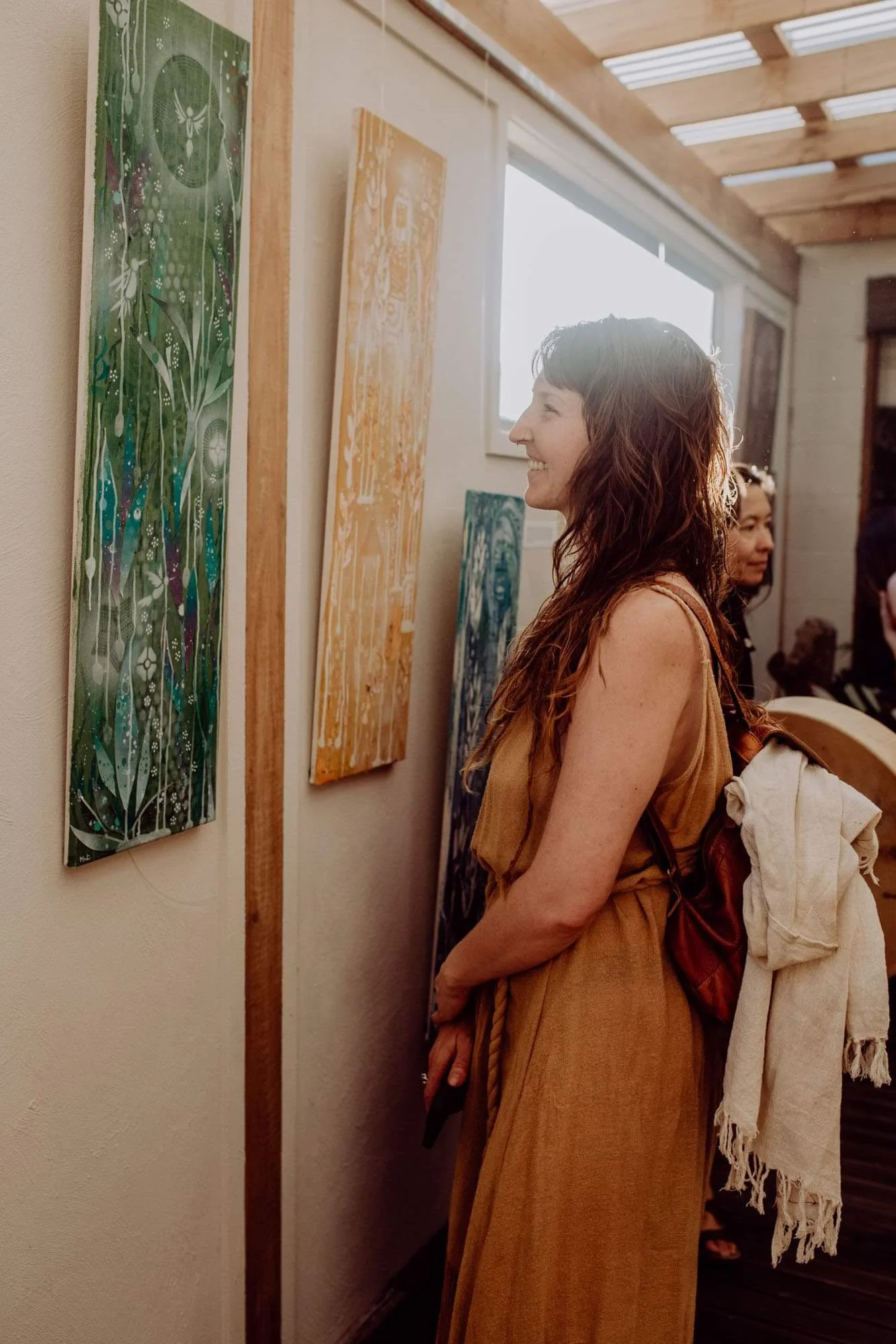 Woman with wavy brown hair admiring colorful abstract paintings at an art gallery.