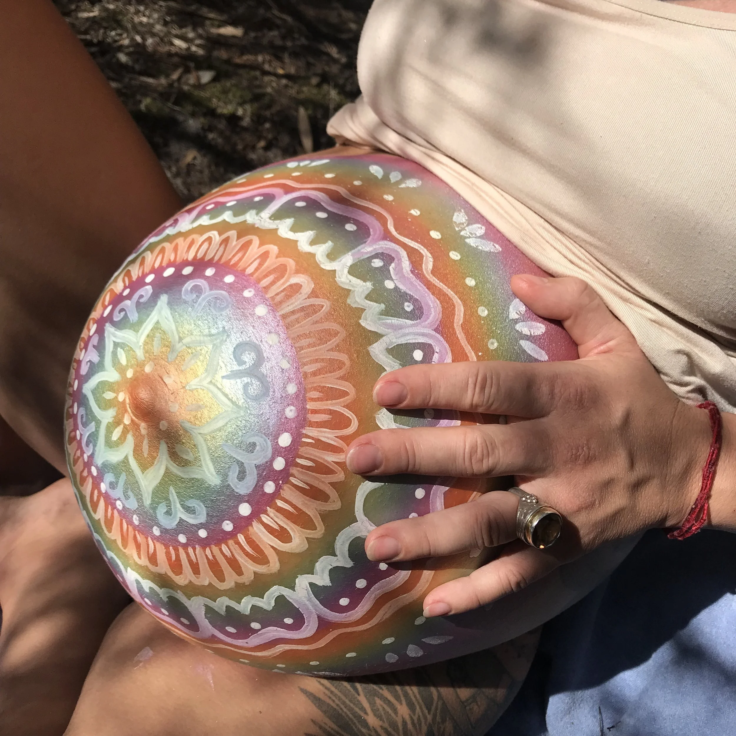 A pregnant lady holding a decorated baby bump painted with colourful mandala-like designs and patterns.