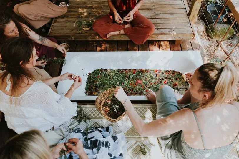 Group of women making a herbal bath with herbs and flowers on a wooden deck.